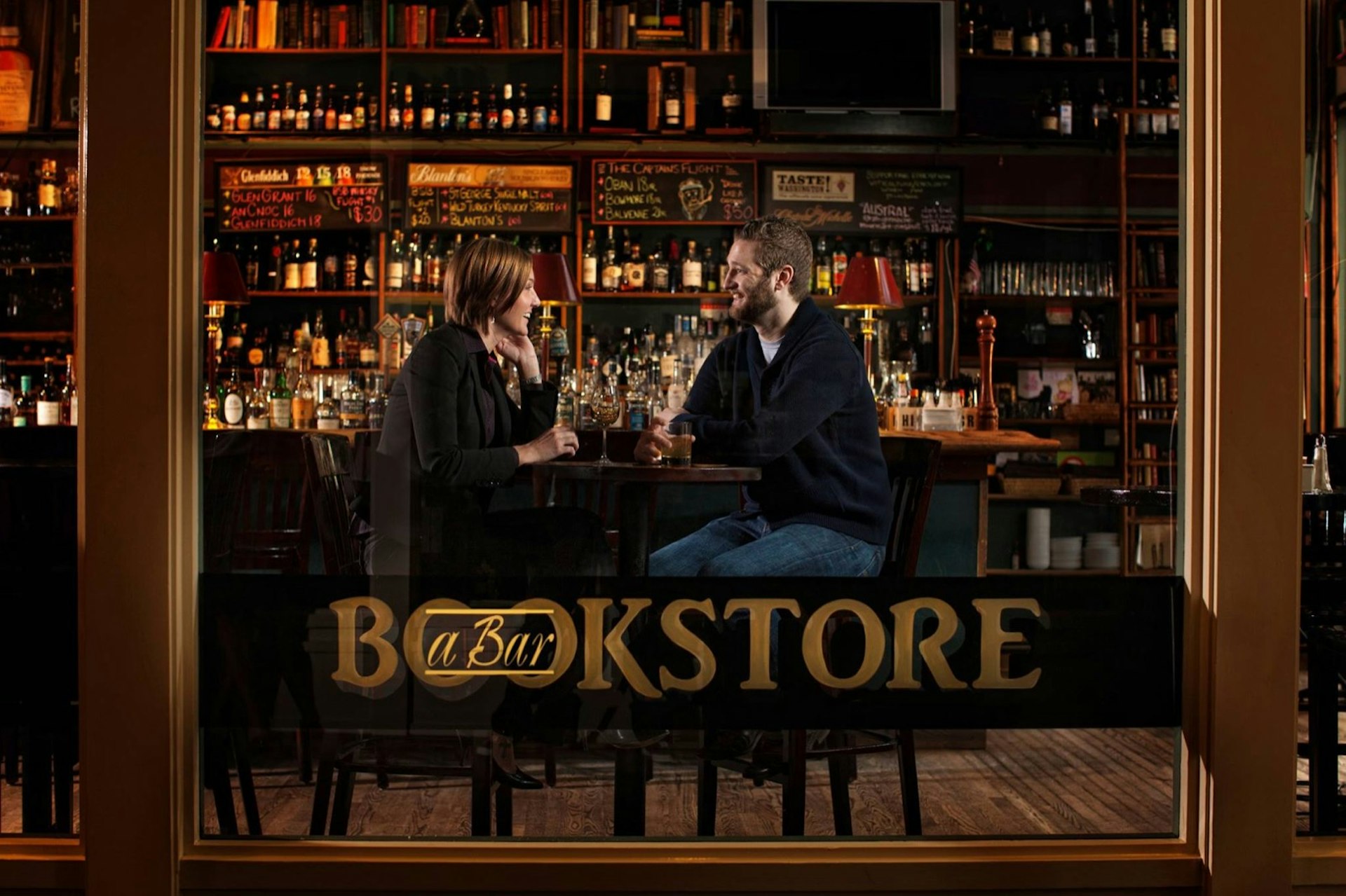 We see two people having drinks in a bar through the large front window, with the name Bookstore written on it. Perfect weekend in Seattle