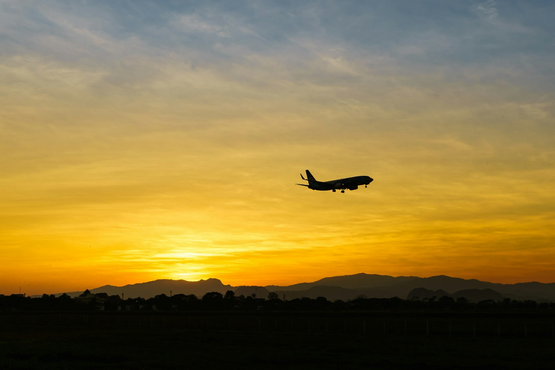 An orange and yellow horizon with a silhouette of a plane flying in the sky.