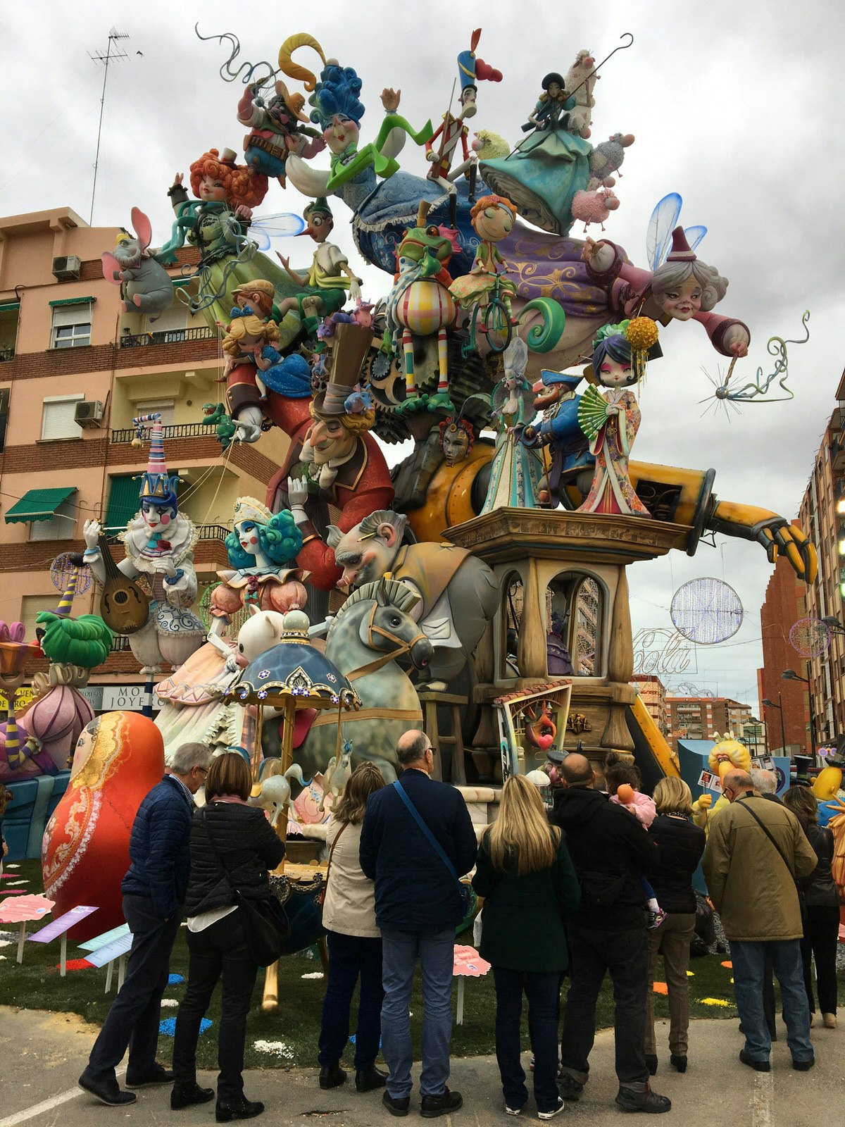 A group of people surrounding a tall falla monument and looking at the many colourful figures with a fairytale theme