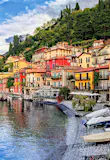 The village of Menaggio on Lake Como, one of the best day trips from Milan; it is a collection of colourful houses, mostly red and yellow, teetering on a green hillside next to the lake, while the shore is lined with boats and there is another boat on the water.