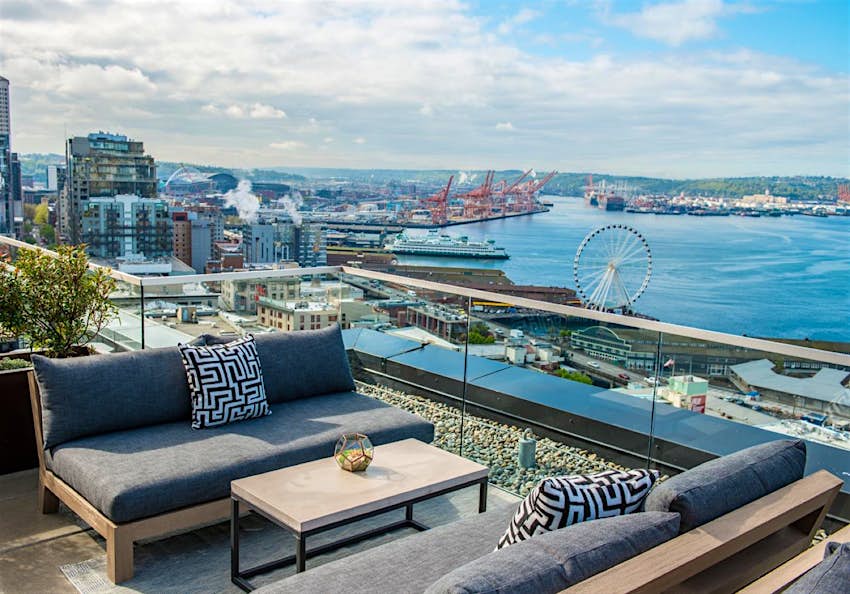 Modern couches and a coffee table are set up on a glass-walled, open air patio on top of a tall building on the Seattle waterfront. Perfect weekend in Seattle