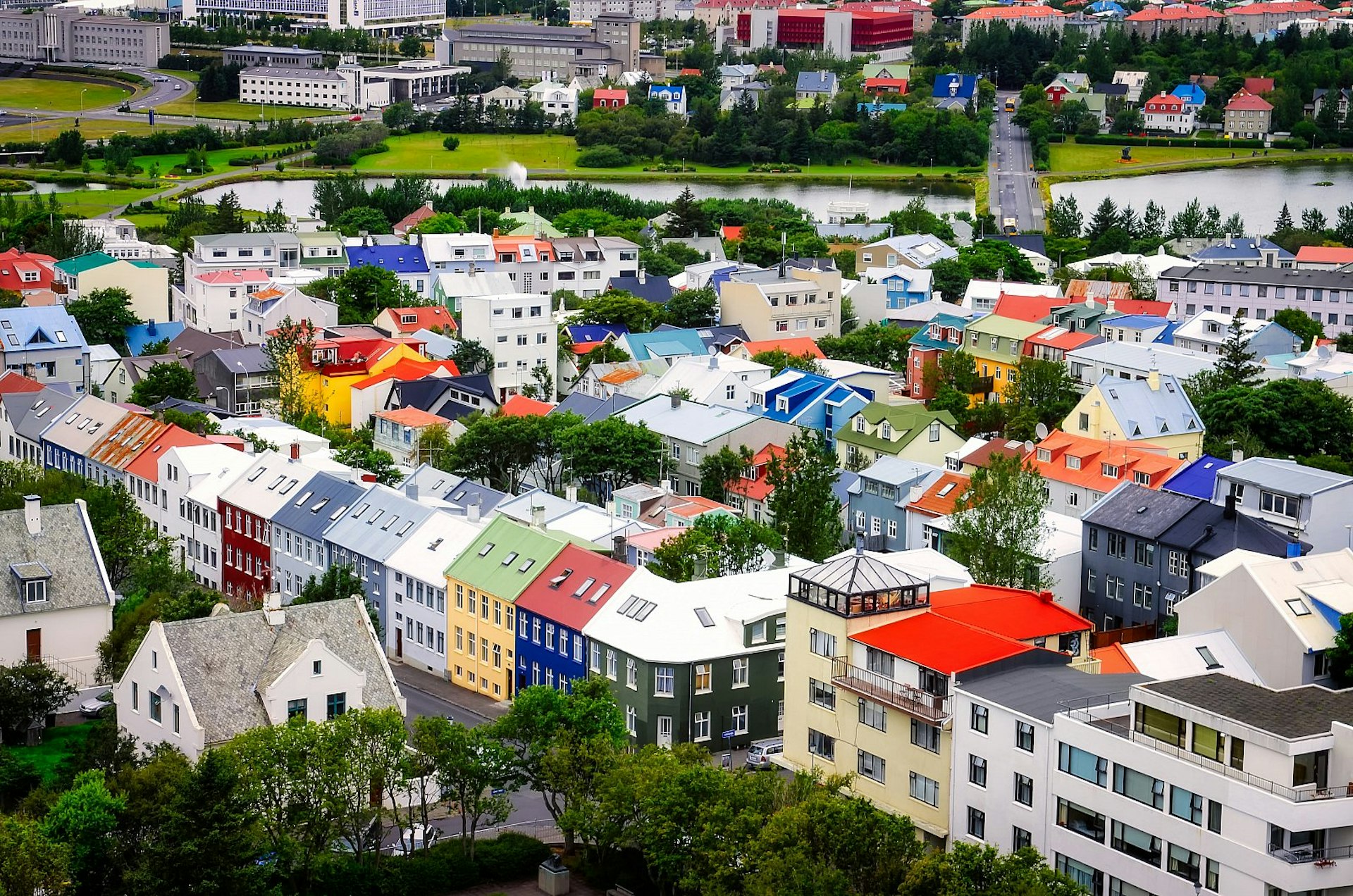 Aerial view of a cluster of colourful houses in a leafy neighbourhood in Reykjavík, Iceland, with a river in the distance.