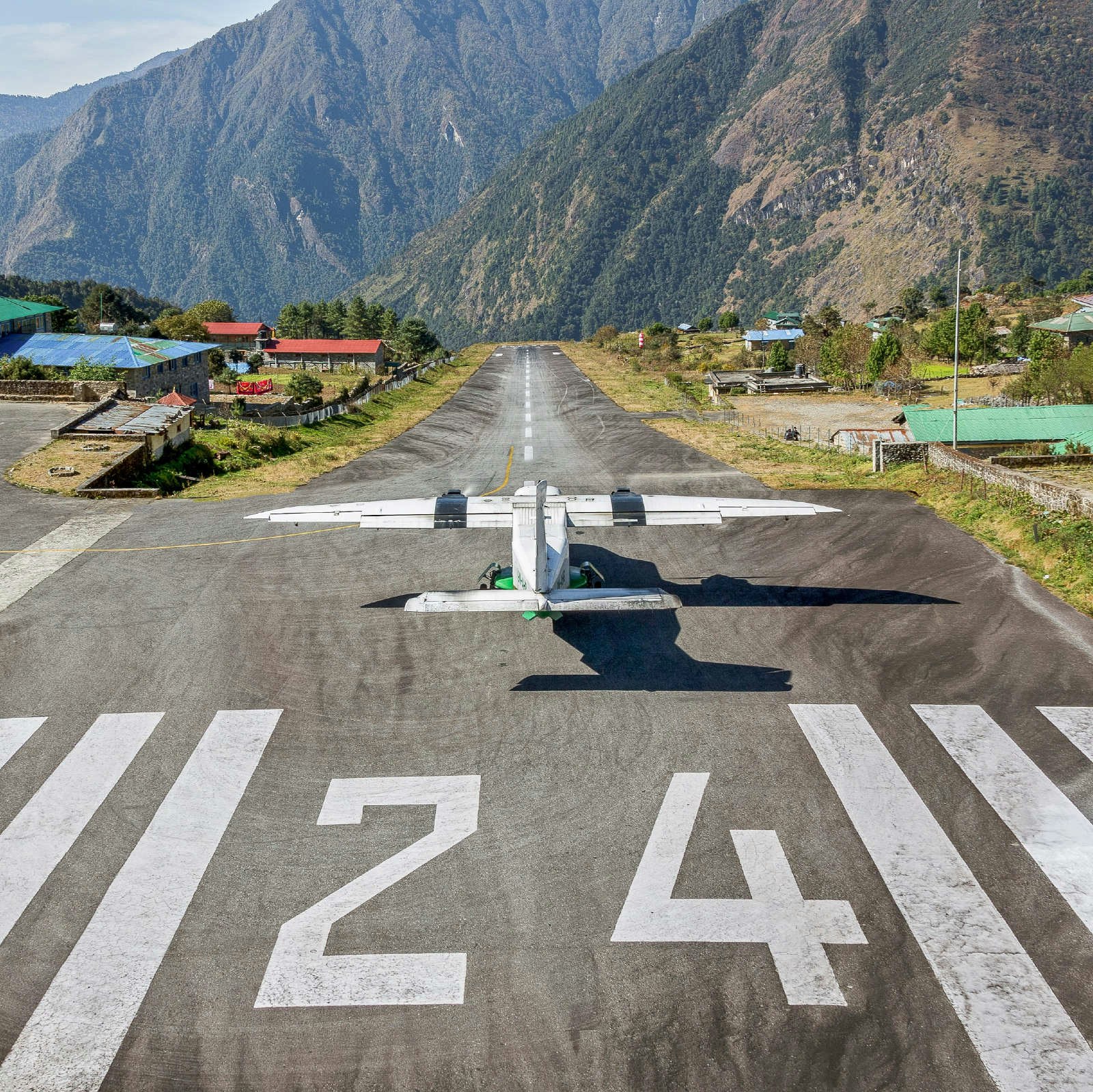 A small plane rests on the narrow, short airport of enzing-Hillary airport in Lukla, Nepal with mountains rising ahead of it.