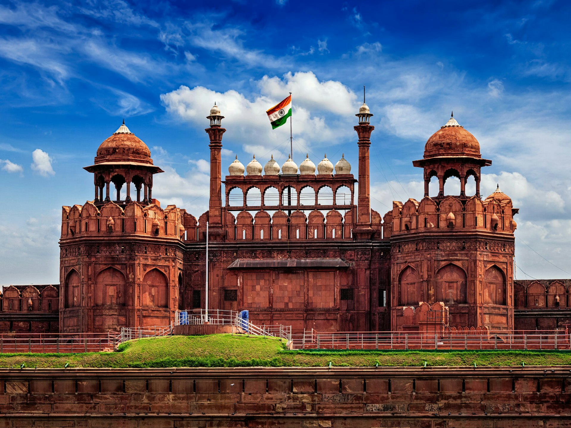 The Indian flag flies over the battlements of a large red-coloured fort with several turrets
