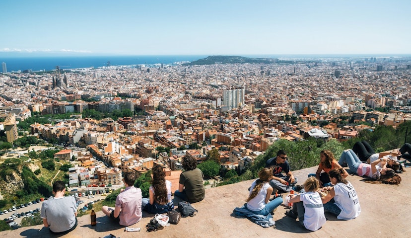 Teens sit on the viewpoint with a view of the city of Barcelona stretching off into the distance