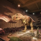 A large T-Rex stands in an empty gallery with light effects creating a sense of being in a prehistoric world