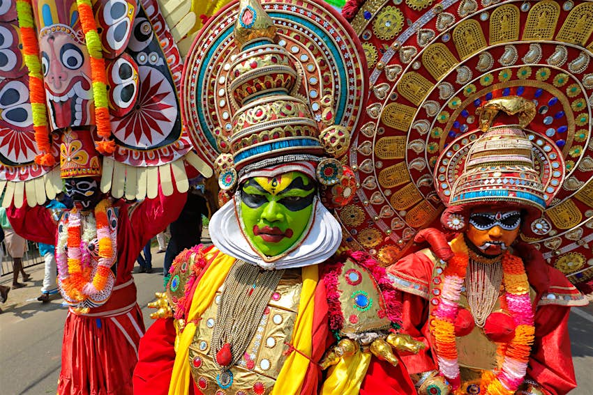 Masked dancers at a Theyyam ceremony in Kannur, India. The dancers have painted faces, flamboyant red outfits, and huge, decadent hats coloured in silver and gold.