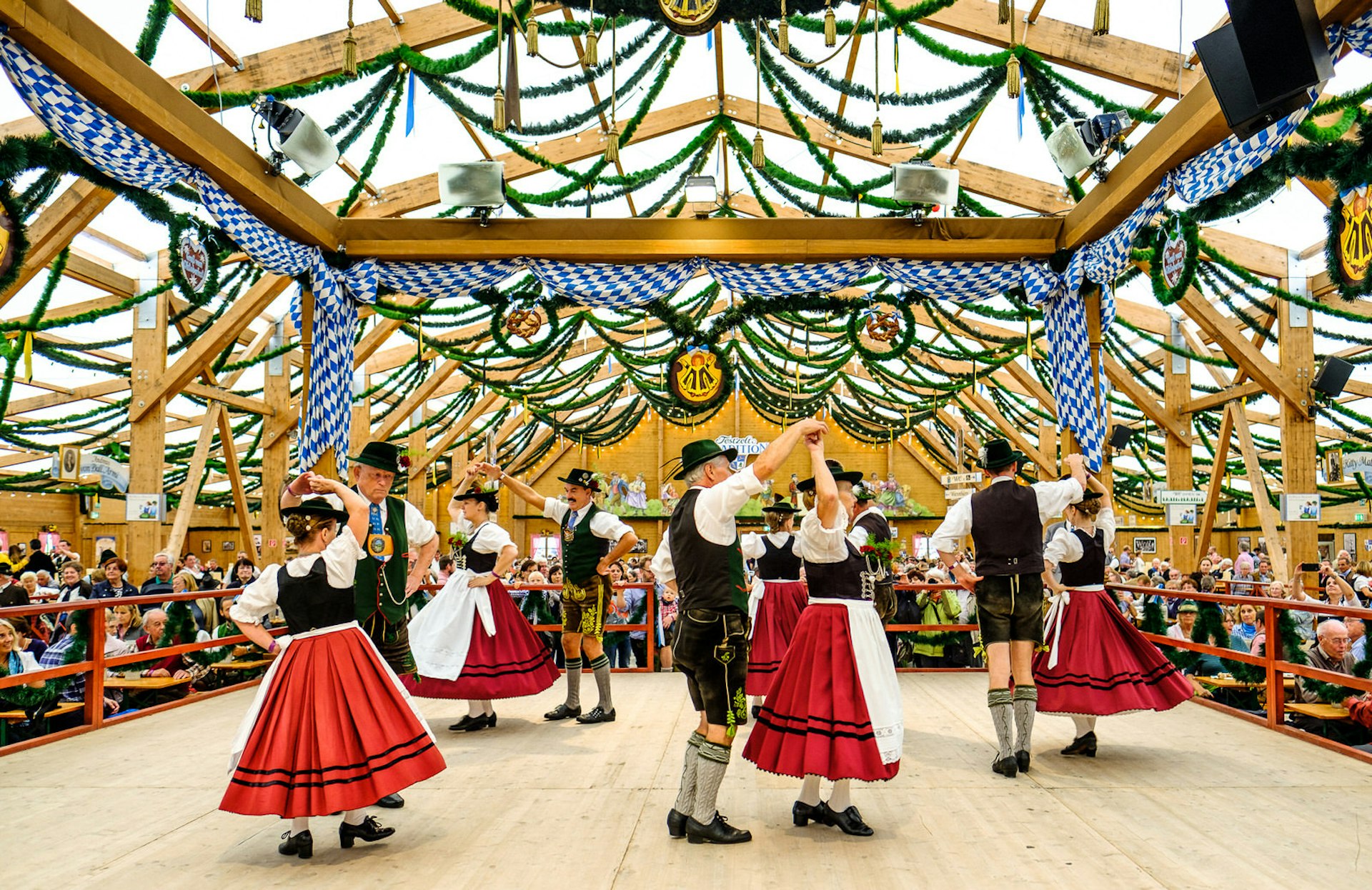 Couples dancing in traditional costumes inside a beer tent during Oktoberfest.