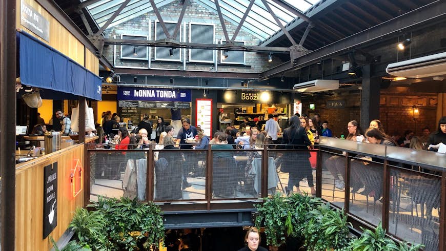 Several diners sit at tables below a glass roof in Victoria's Market Hall