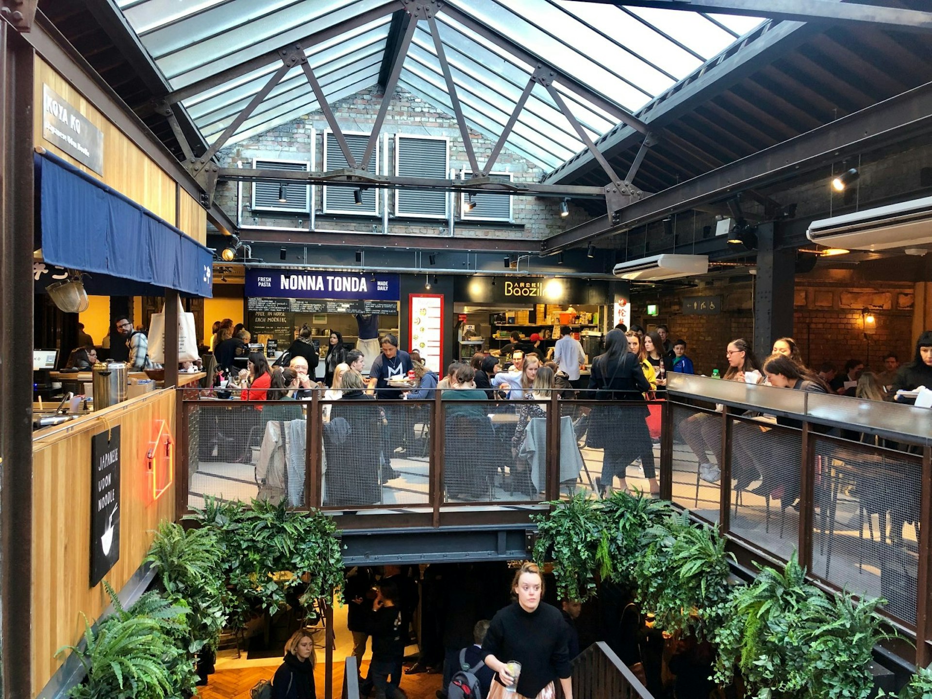 Several diners sit at tables below a glass roof in Victoria's Market Hall