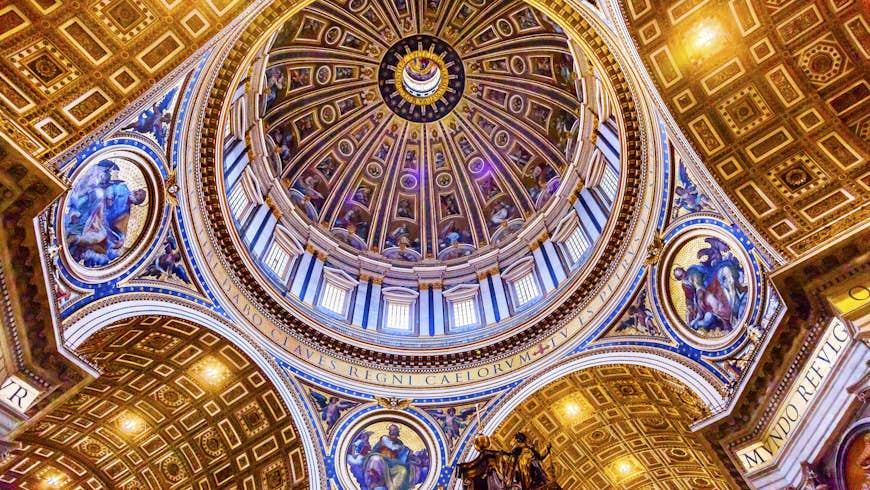 Looking upwards, the image shows a huge circular dome surrounded by windows; large semi-circular vaulted ceilings glistening in gold gilding branch off from the bottom of the dome in four directions