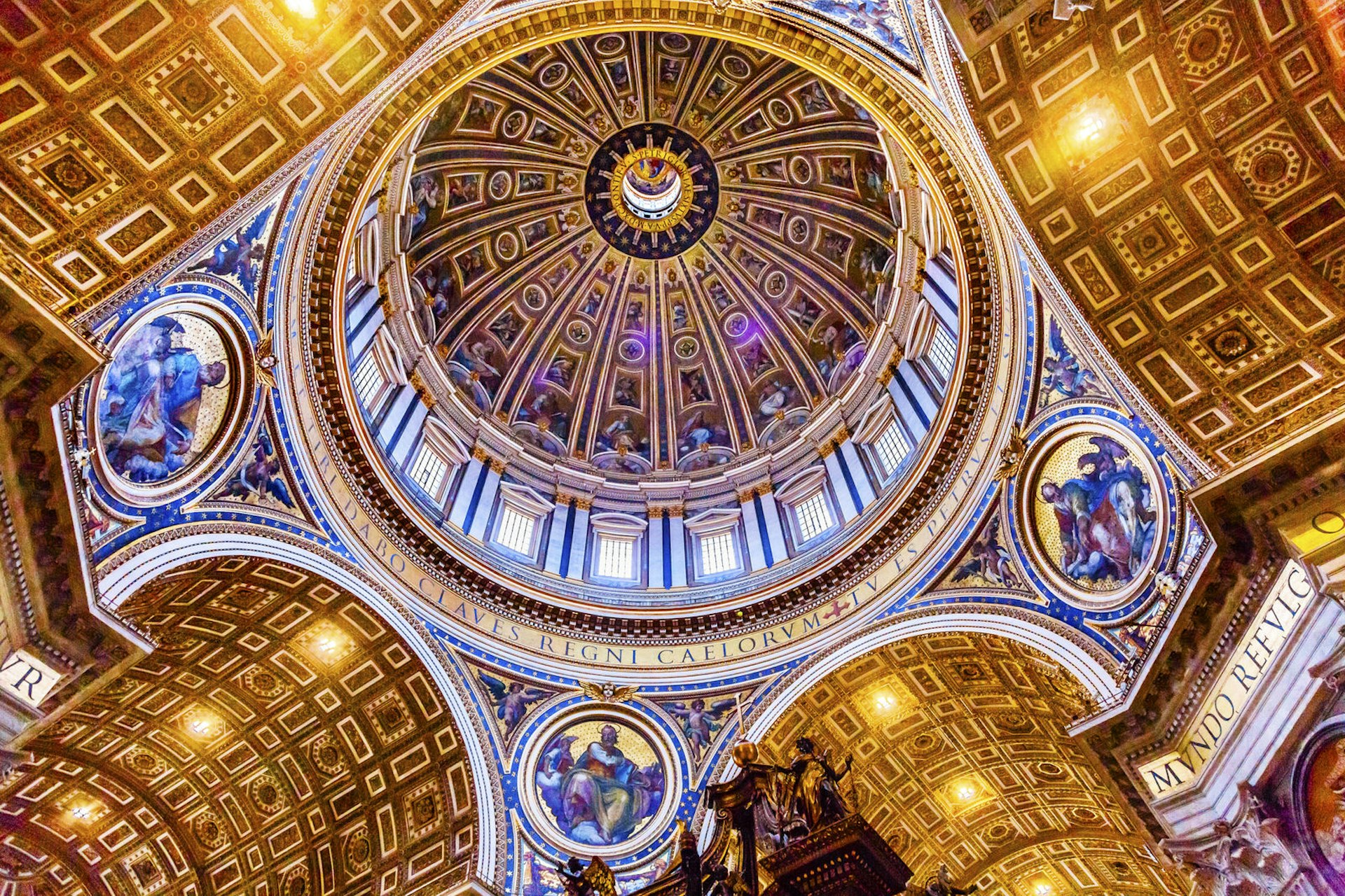 Looking upwards, the image shows a huge circular dome surrounded by windows; large semi-circular vaulted ceilings glistening in gold gilding branch off from the bottom of the dome in four directions