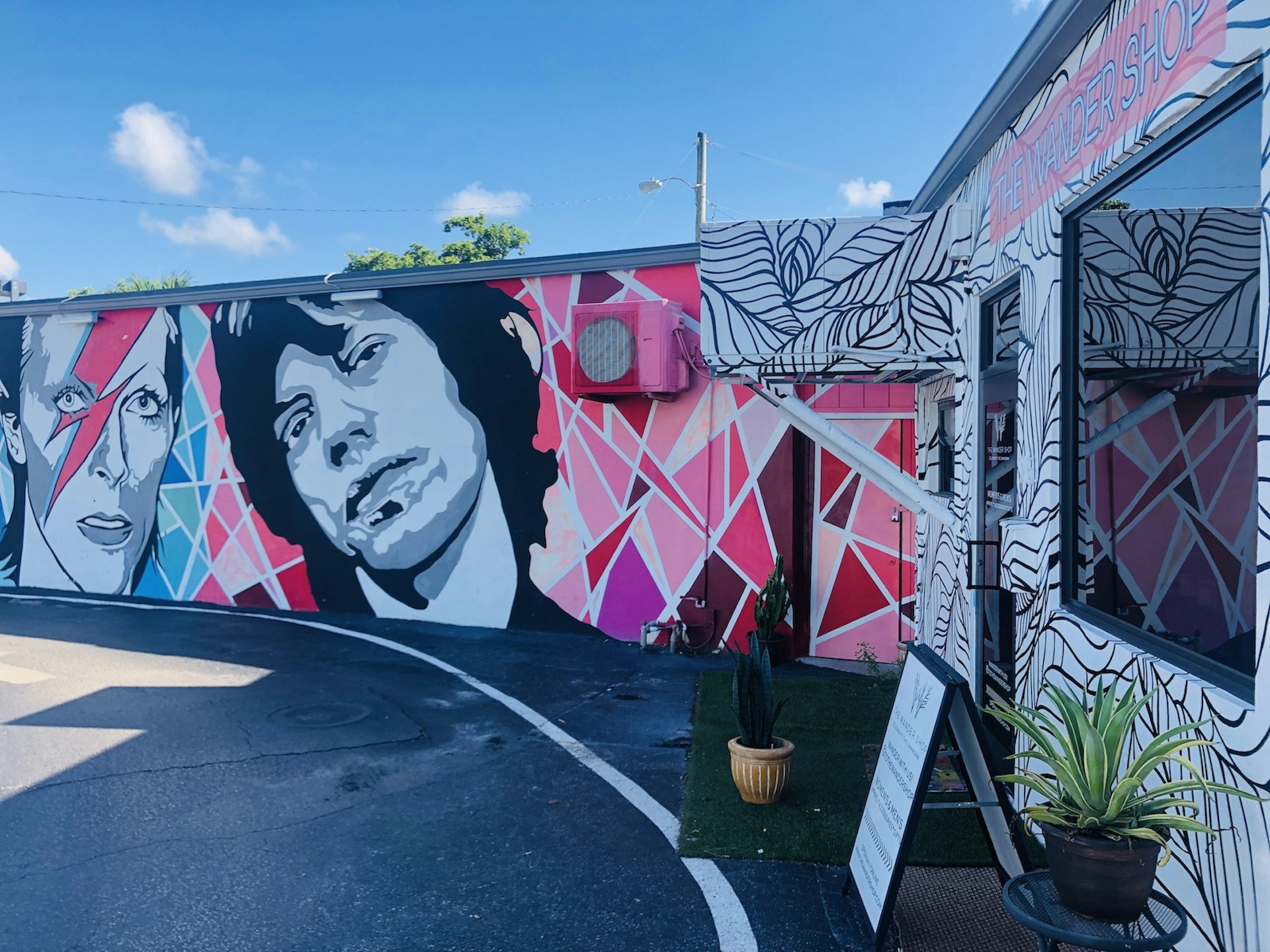 A mural of David Bowie and Mick Jagger in pink, grey and purple shades covers a wall next to a small boutique.