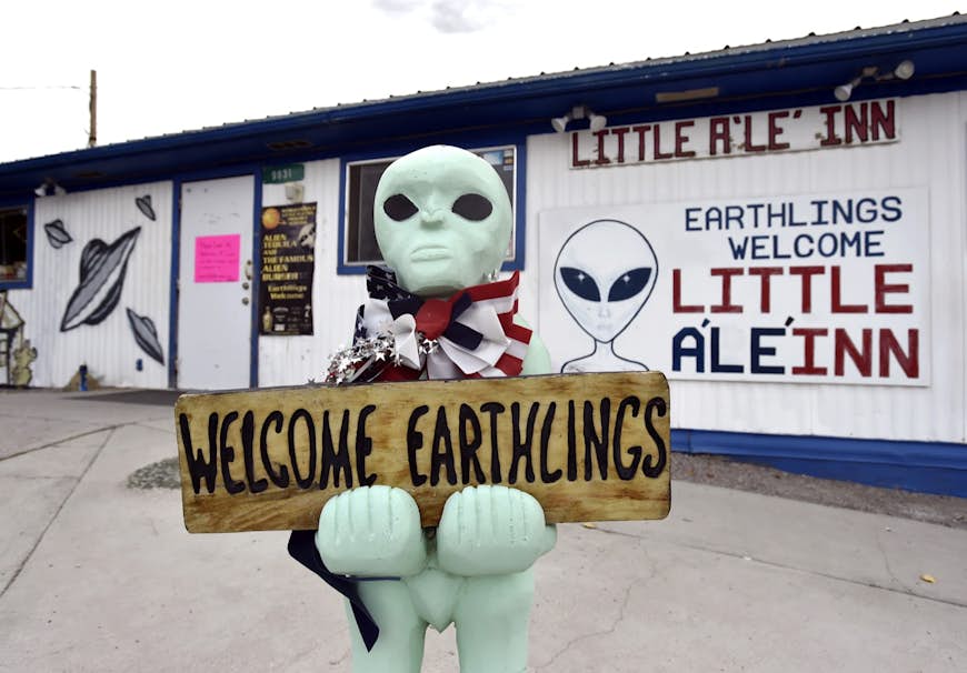 A plastic green alien holds a sign that says "welcome earthlings" in front of Little A'LE' INN in Nevada; there are plenty of quirky spots along the way to Area 51.