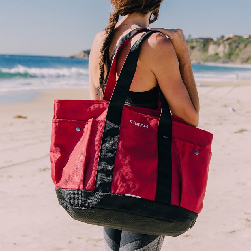 En kvinna som rymmer en röd tygpåse på en strand;  strandutrustning
