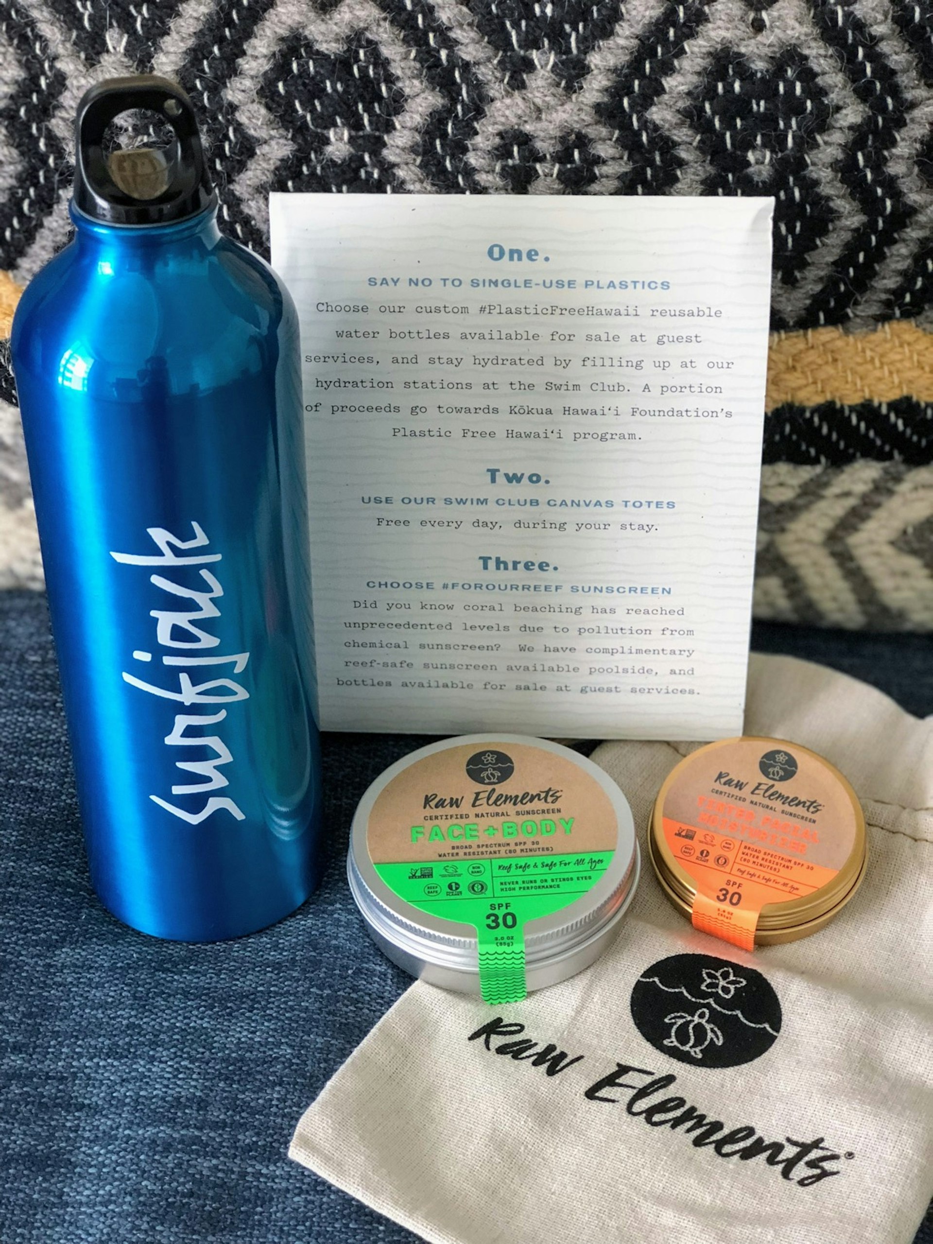 Gear including a reusable water bottle, reef safe sun products and a reusable canvas bag are shown with a letter offering ideas for sustainable travel
