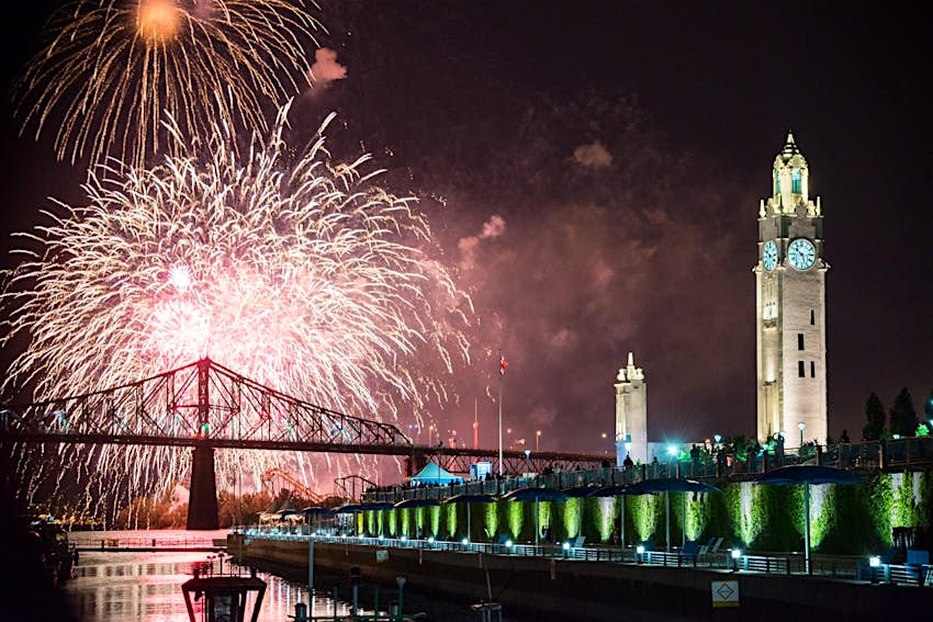 Fireworks explode in the sky over a bridge and iconic clock tower. The International Fireworks Festival is one of the best free things to do in Montréal