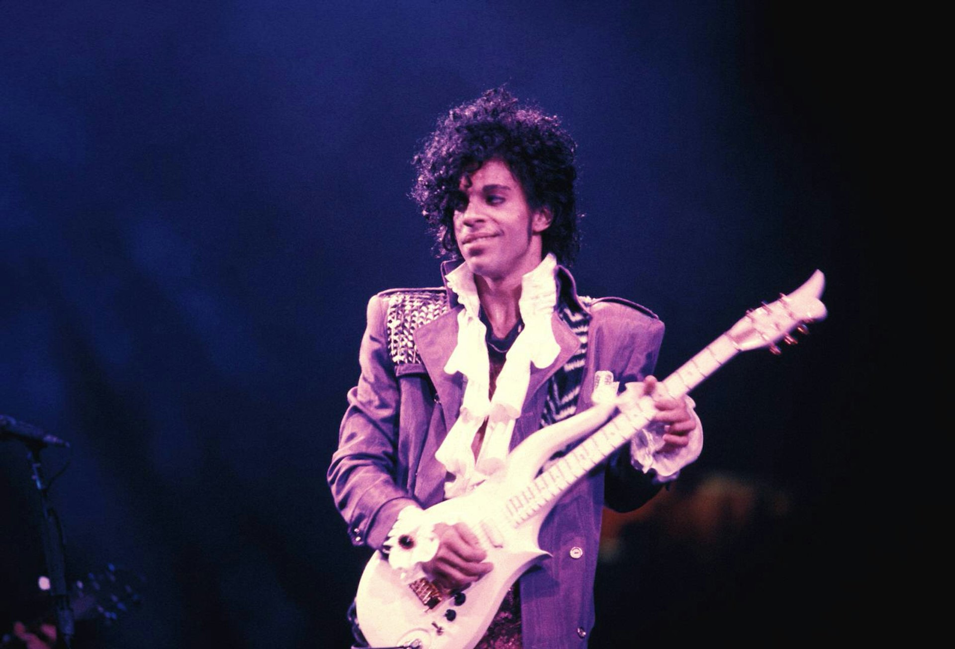 Prince performing on stage at the Ritz Club holding a white electric guitar 