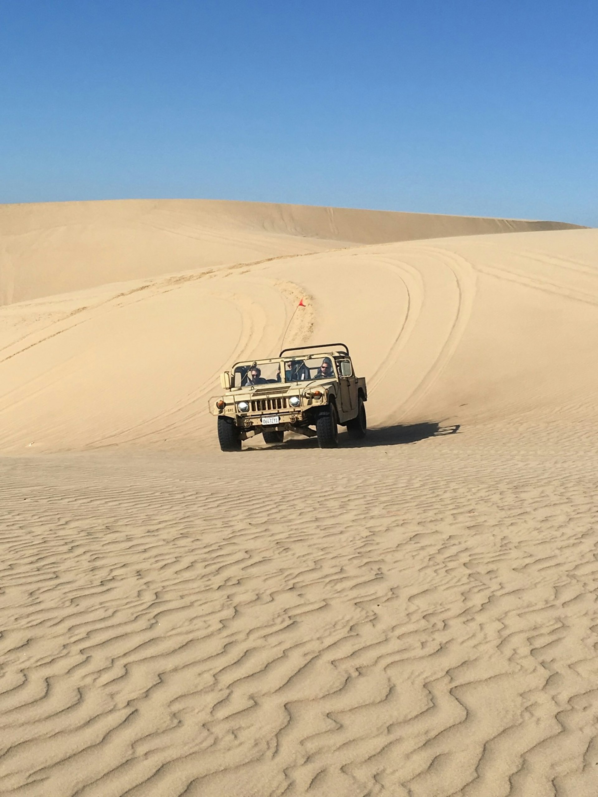 A tan humvee rolls over sand dunes; San Luis Obispo adventures