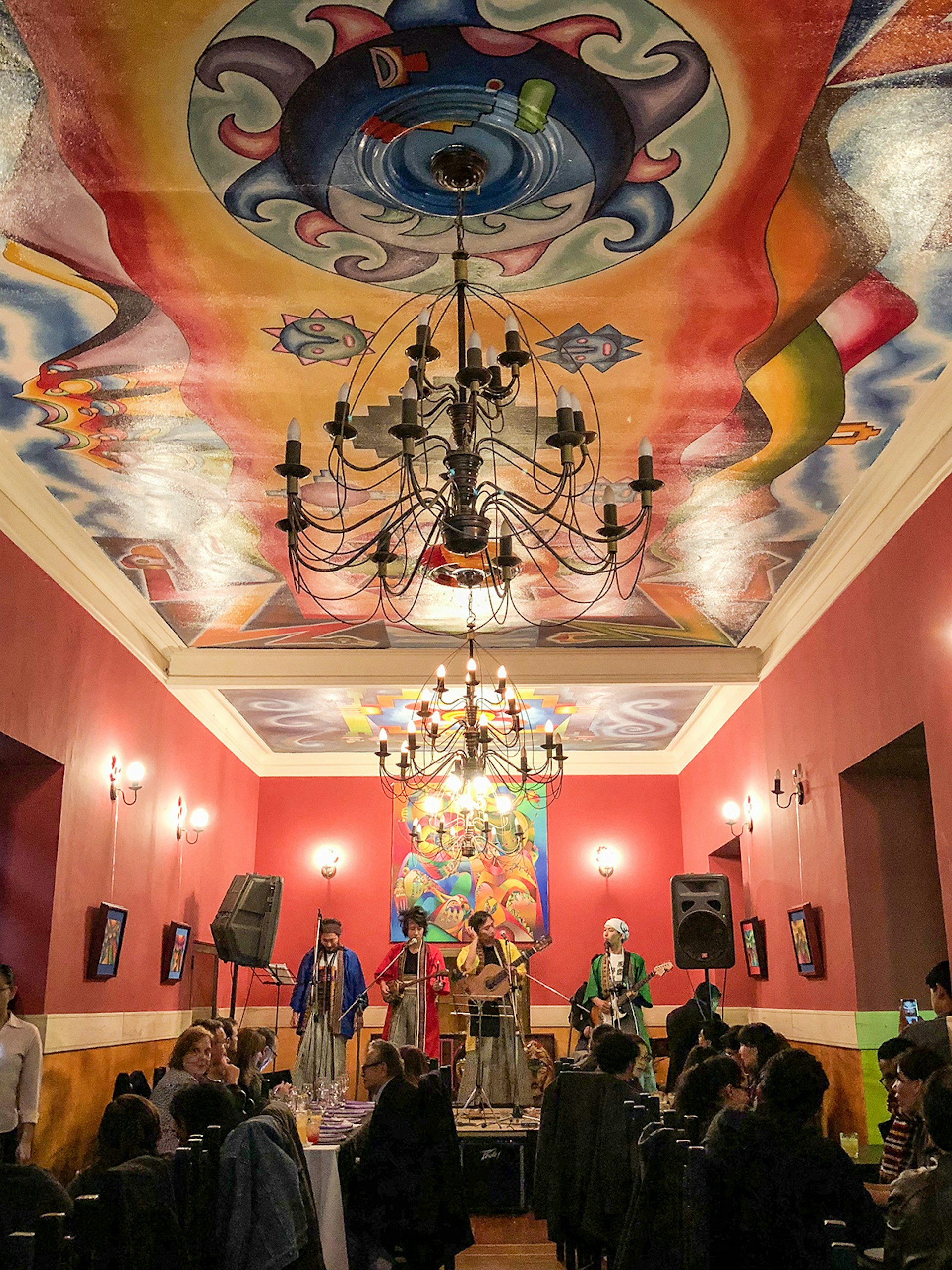 Bolivian musicians play in a red room with a colorful mural on the ceiling. La Paz, Bolivia.