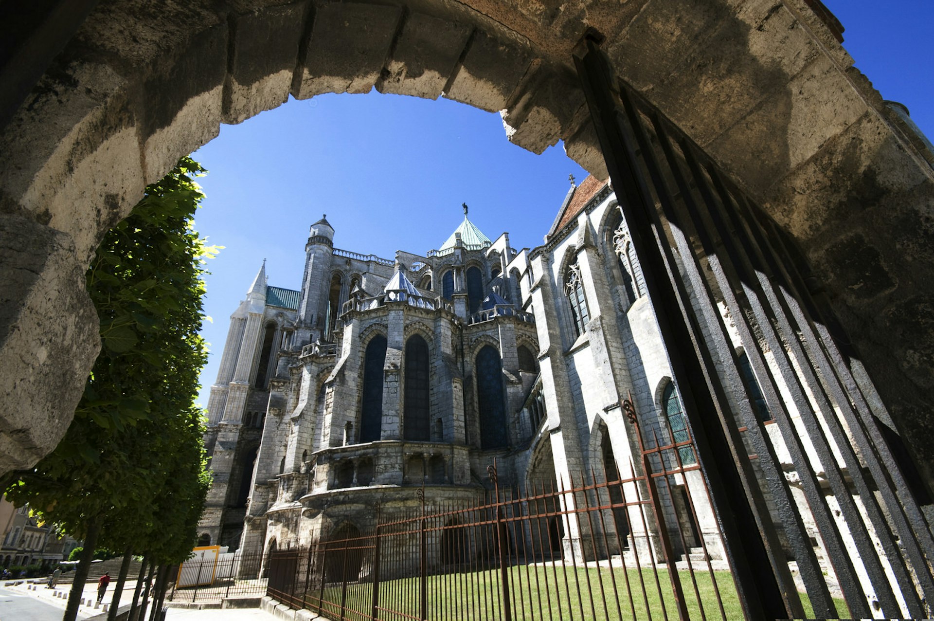 Chartres' Cathédrale Notre Dame as viewed from beneath a stone arch. The cathedral is made from stone in a Romanesque style and has a number of spires.