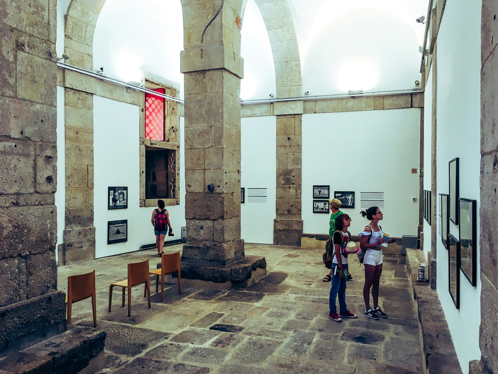 Four people look at various photo exhibits within a large white-washed room within an old prison; large stone columns and arches dominate the space; free things to do in Porto