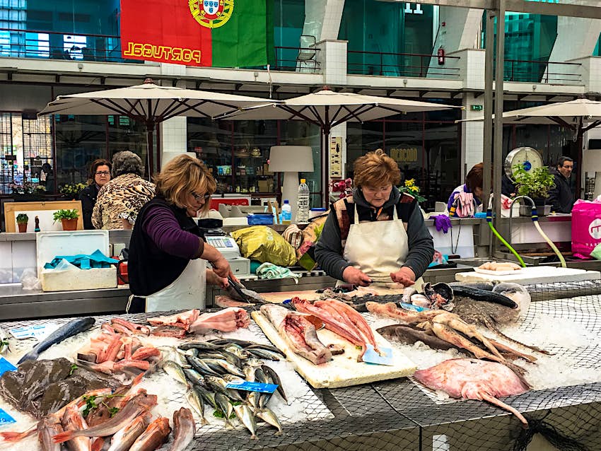 Features - Mercado de Matosinhos Two women working at a fishmonger stall clean fish at Mercado de Matosinhos; visiting this local market is one of the best free things to do in Porto