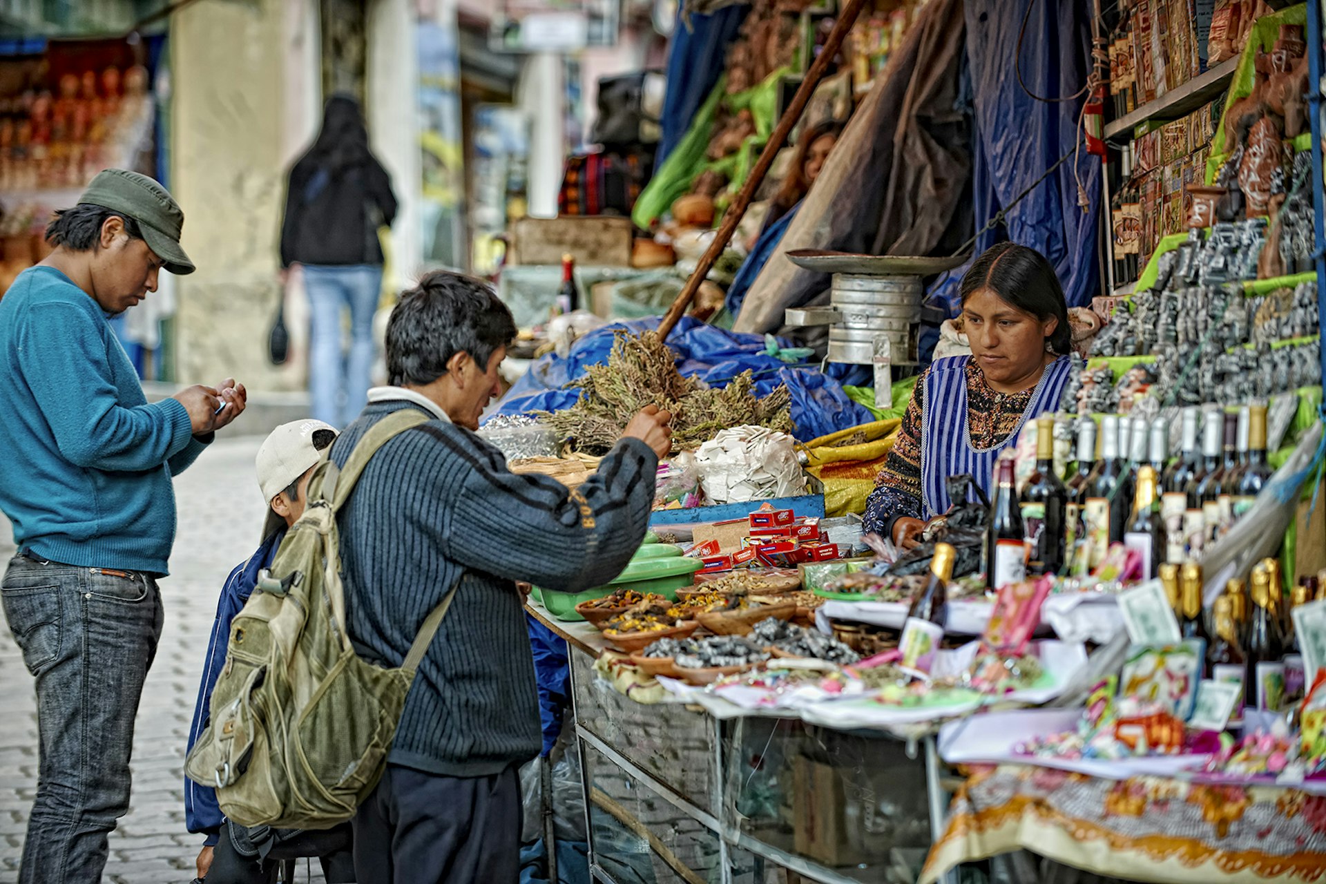 En försäljare på Mercado de las Brujas pratar med en man om hennes varor.  Boden är kantad med talismaner och örter.  La Paz, Bolivia.