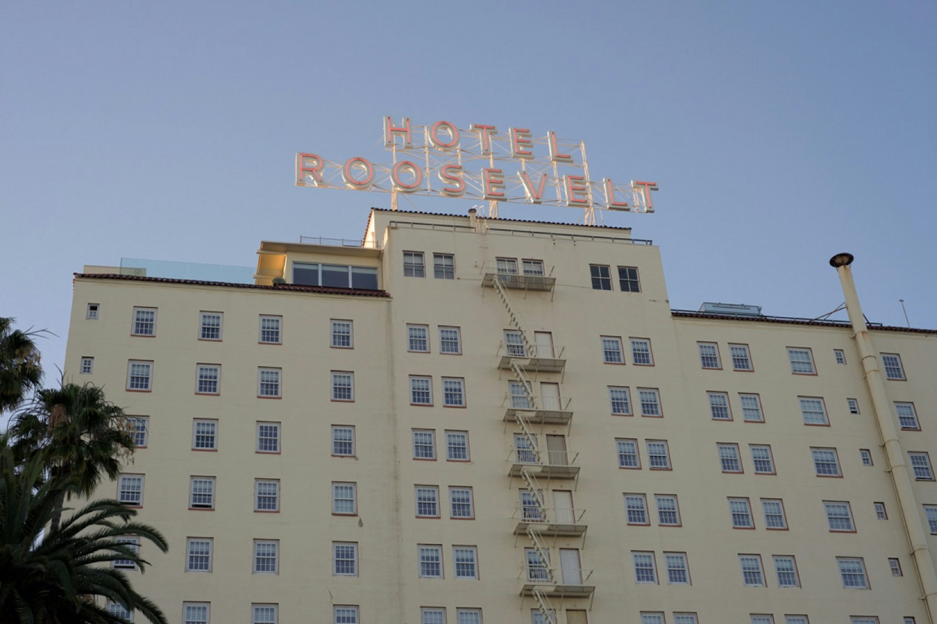 On top of a white hotel building is a neon sign identifying it as the Hotel Roosevelt, but it's daytime so the neon light is not lit; Los Angeles neon