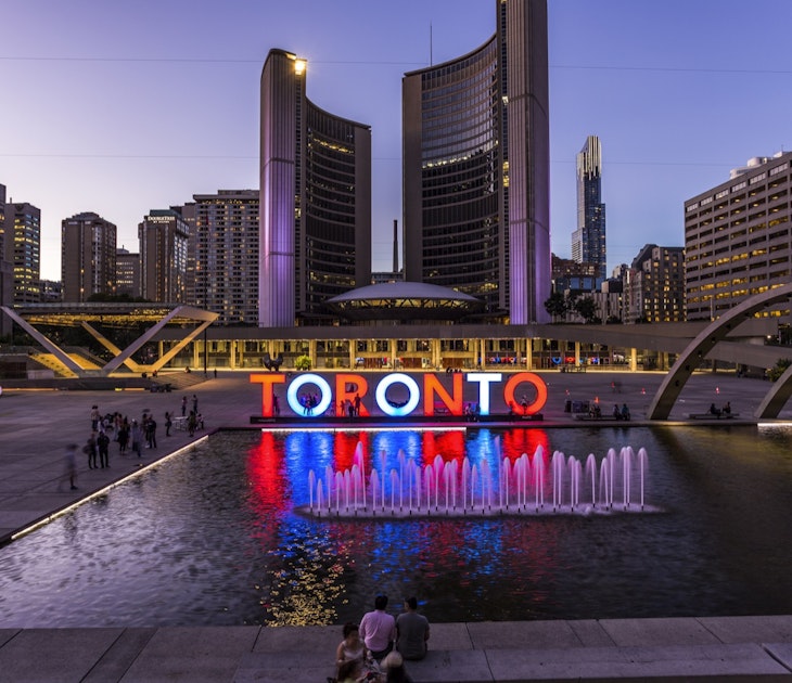 The Toronto sign at Nathan Phillips Square is lit up in red and white and blue, and reflected in a pool, as the sun goes down in Toronto; Weekend in Toronto