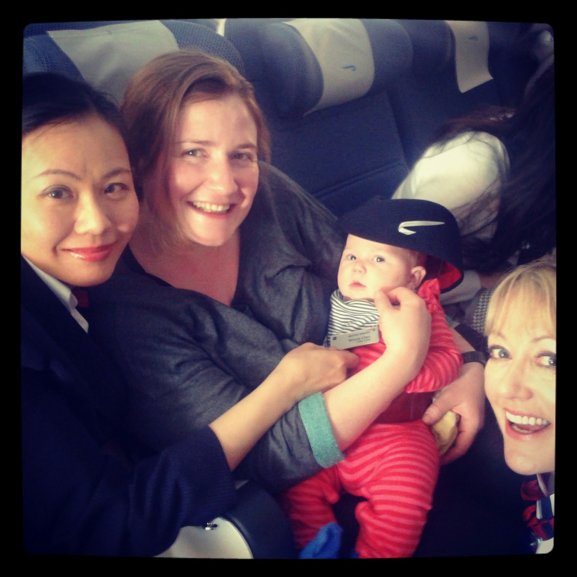 The writer sits with her baby in an airplane seats, flanked by two female air stewards smiling for the camera.
