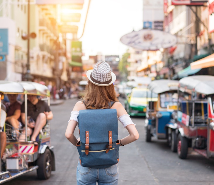 The back of a young woman walking along the pedestrian street in the evening in Bangkok, Thailand; travelers, tourists and tuktuks line the street.
