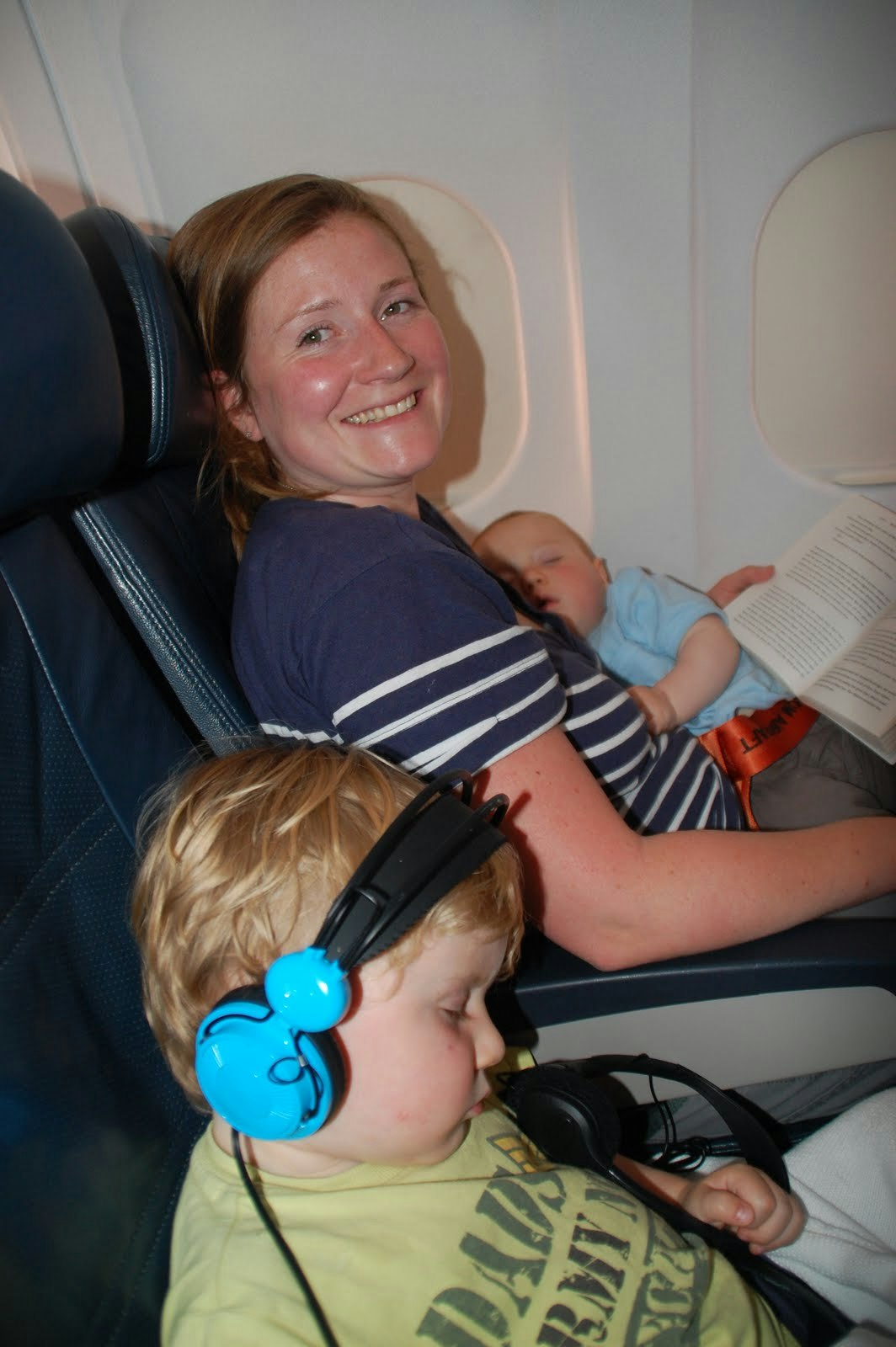 Imogen cradles a baby in her arms while another child rests on the seat listening to headphones