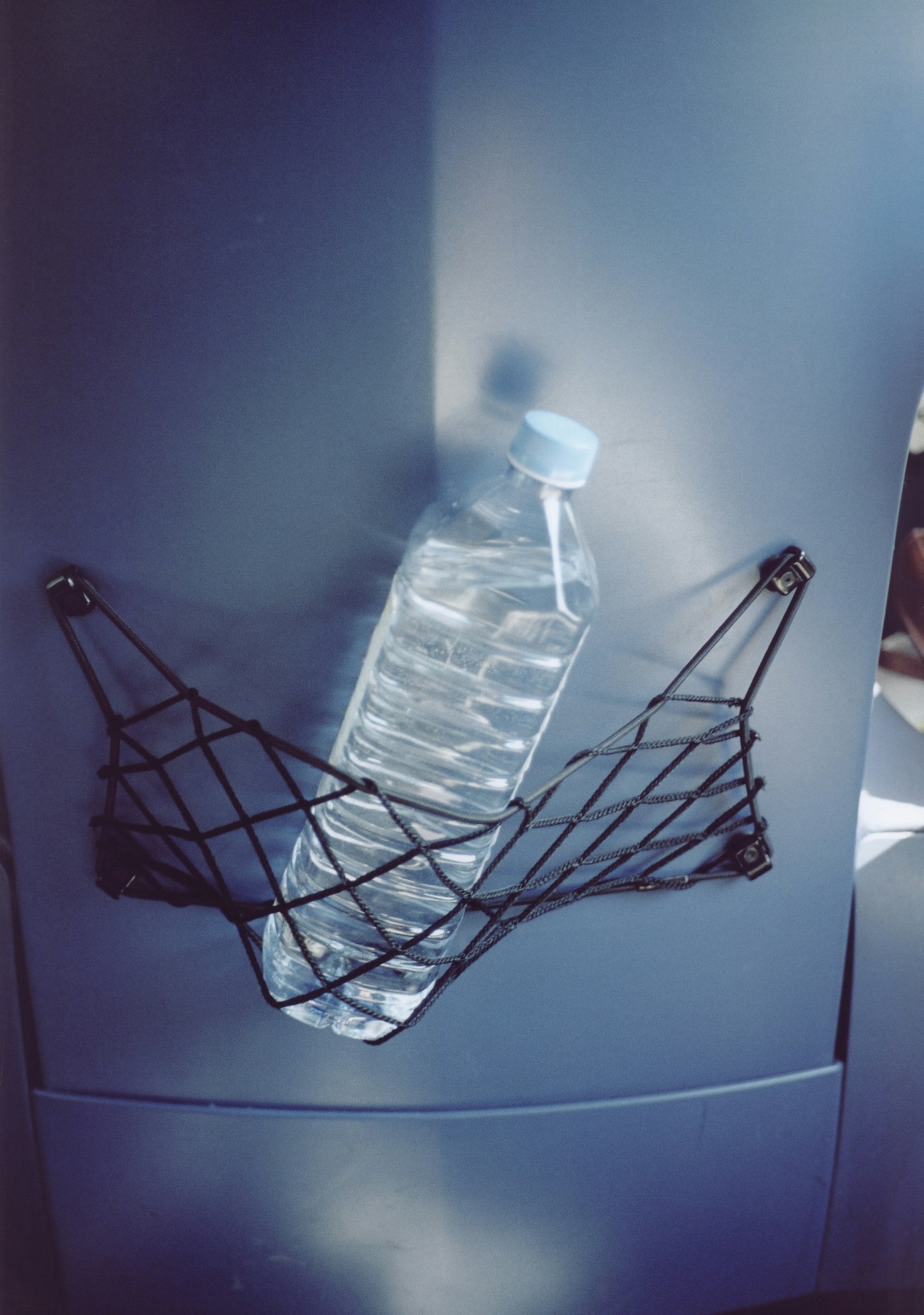 An unbranded clear plastic bottle sits in the netting on the back of a plane seat. It's full of water. Keeping hydrated can reduce jet lag.