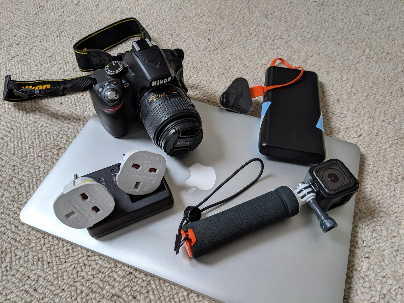 A flat lay of a laptop, plug adaptors, camera and battery pack