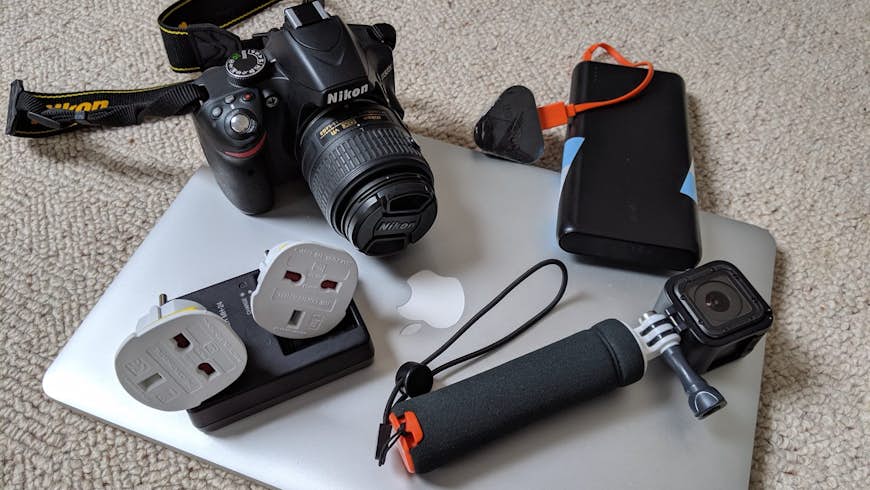 A flat lay of a laptop, plug adaptors, camera and battery pack