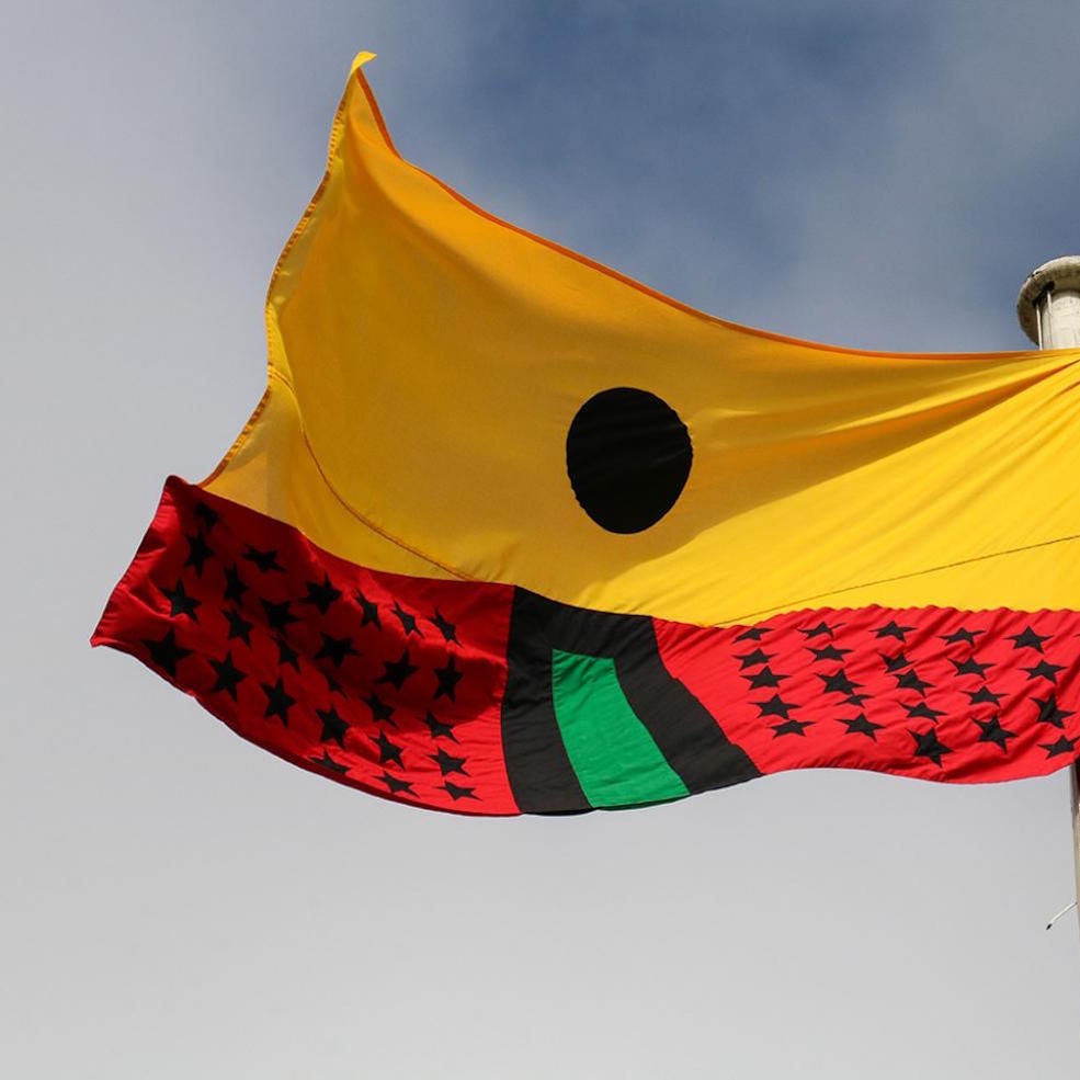 Artist Larry Achiampong's PAN AFRICAN FLAG FOR THE RELIC TRAVELLERS’ ALLIANCE on a flagpole, a red, green, yellow, and black appliqued flag that highlights African diasporic identity