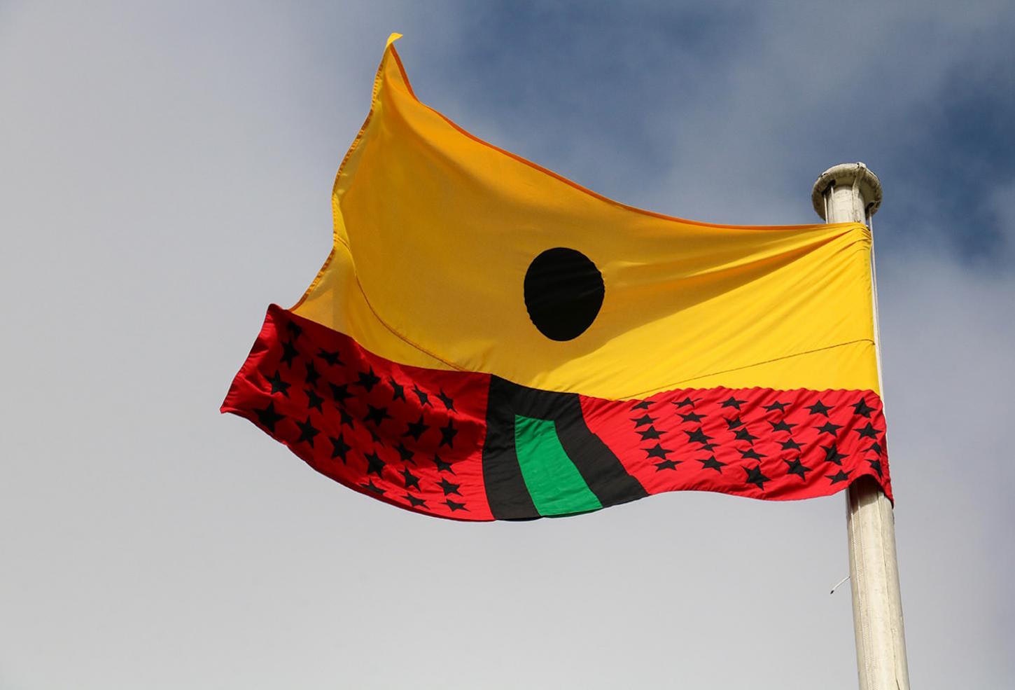 Artist Larry Achiampong's PAN AFRICAN FLAG FOR THE RELIC TRAVELLERS’ ALLIANCE on a flagpole, a red, green, yellow, and black appliqued flag that highlights African diasporic identity