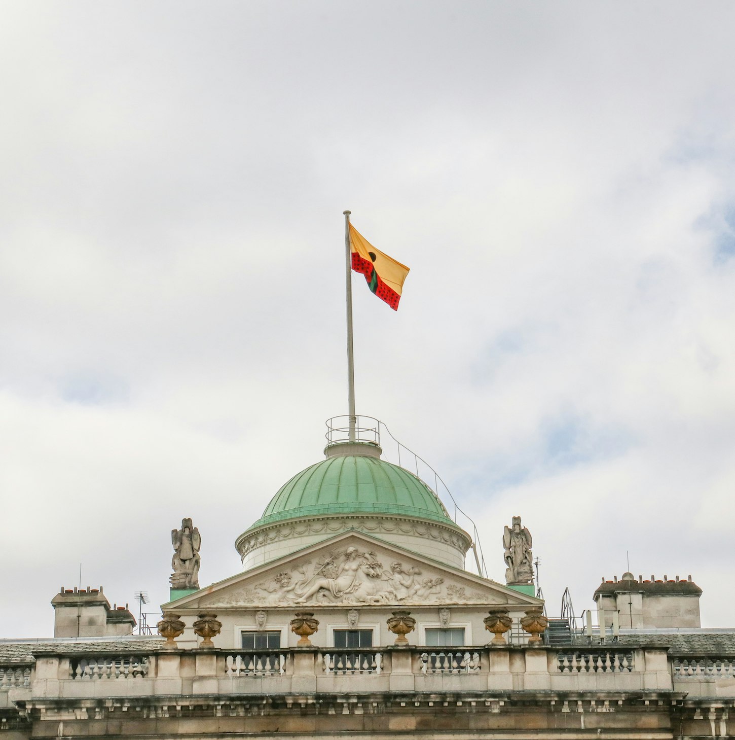 Larry Achiampong's PAN AFRICAN FLAG FOR THE RELIC TRAVELLERS’ ALLIANCE flying over an ornate building with a green dome