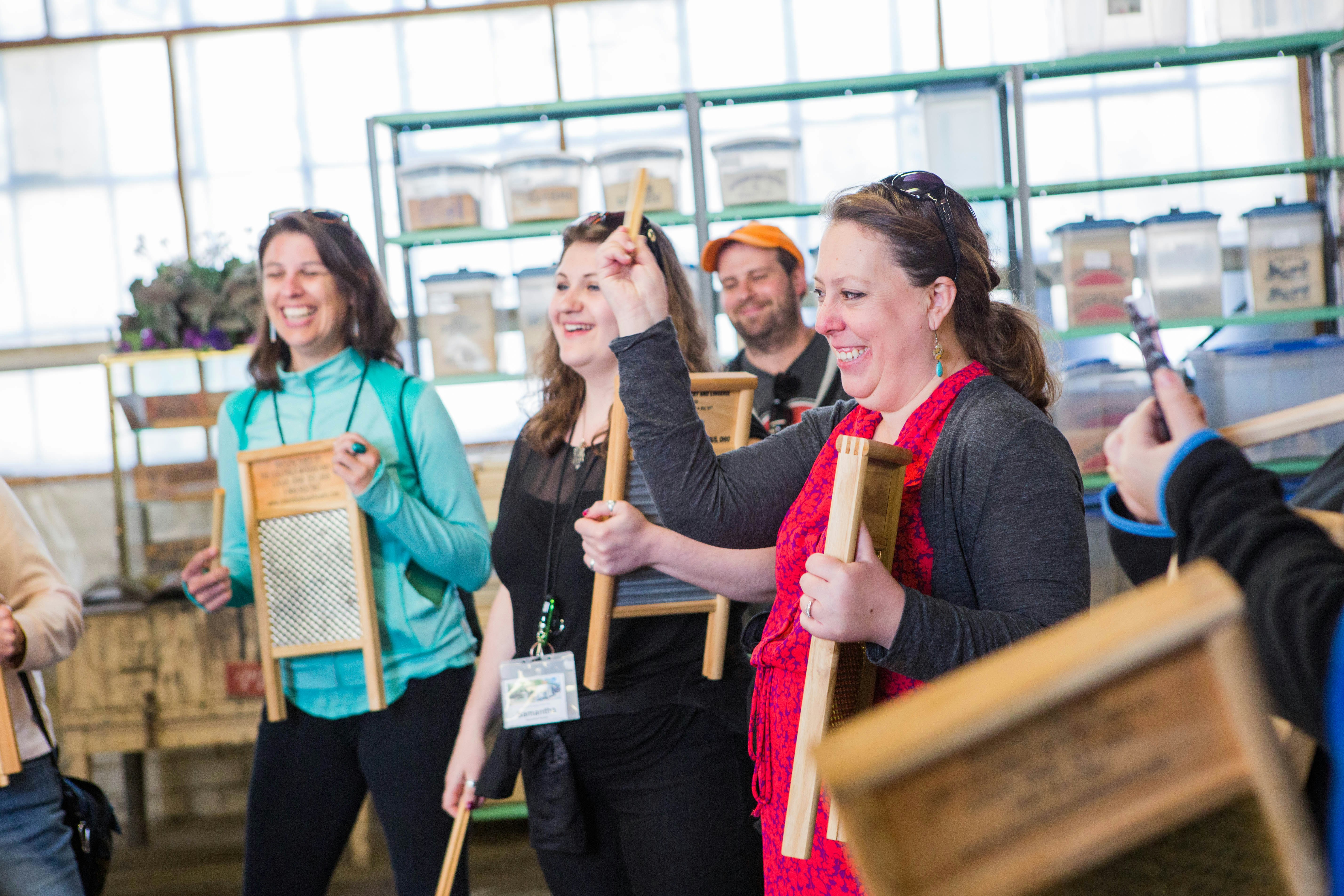 Three women and a man, all smiling and laughing, play washboards as musical instruments at the Columbus Washboard Company as part of their tour of the factory.