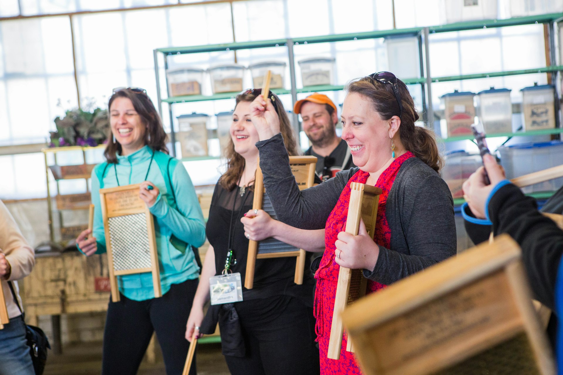 Three women and a man, all smiling and laughing, play washboards as musical instruments at the Columbus Washboard Company as part of their tour of the factory.