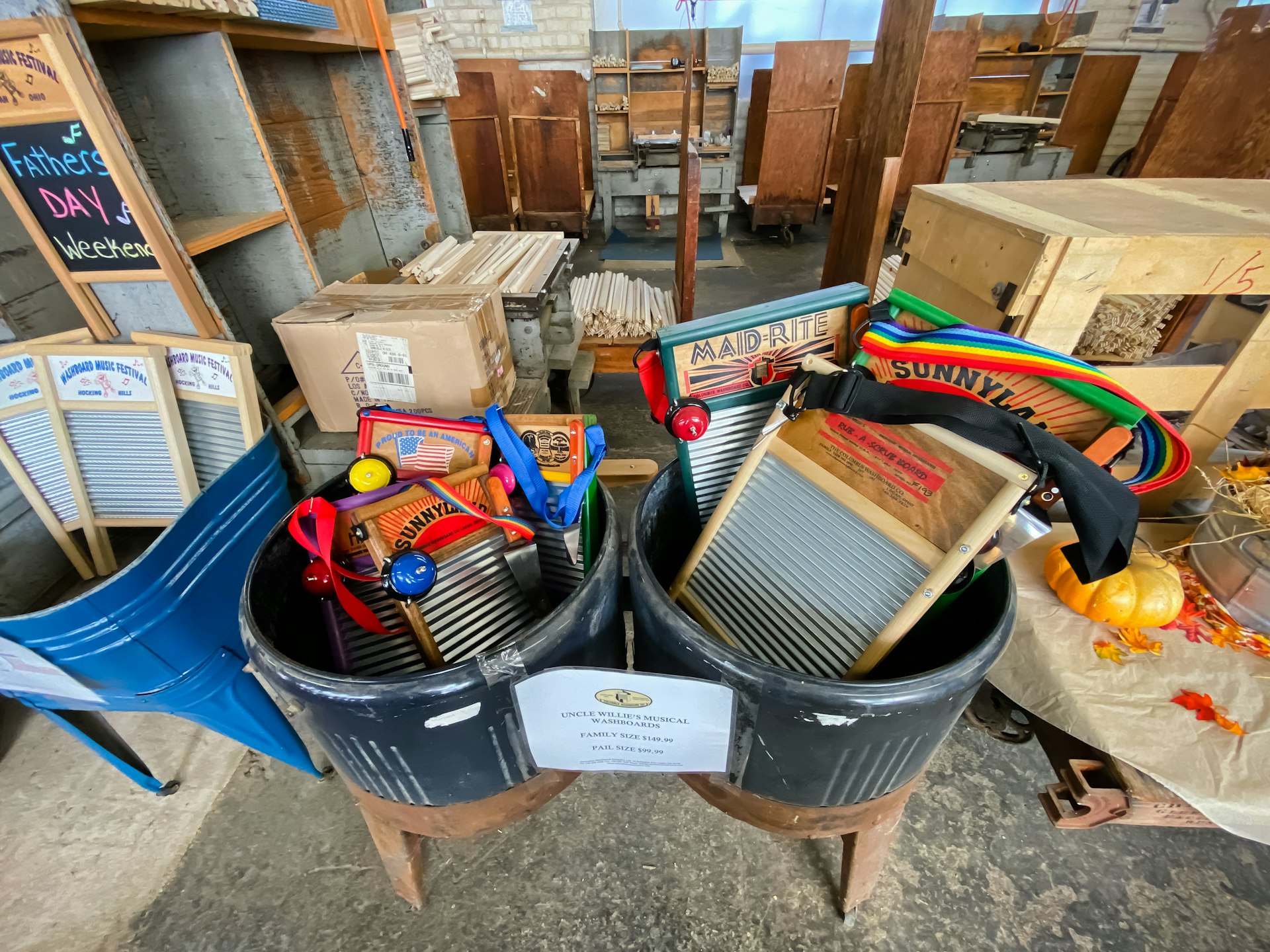 A large metal tub full of washboards outfitted for musical use with bells and colorful neck straps are arranged near a decorative display of fall gourds at the Columbus Washboard Factory.