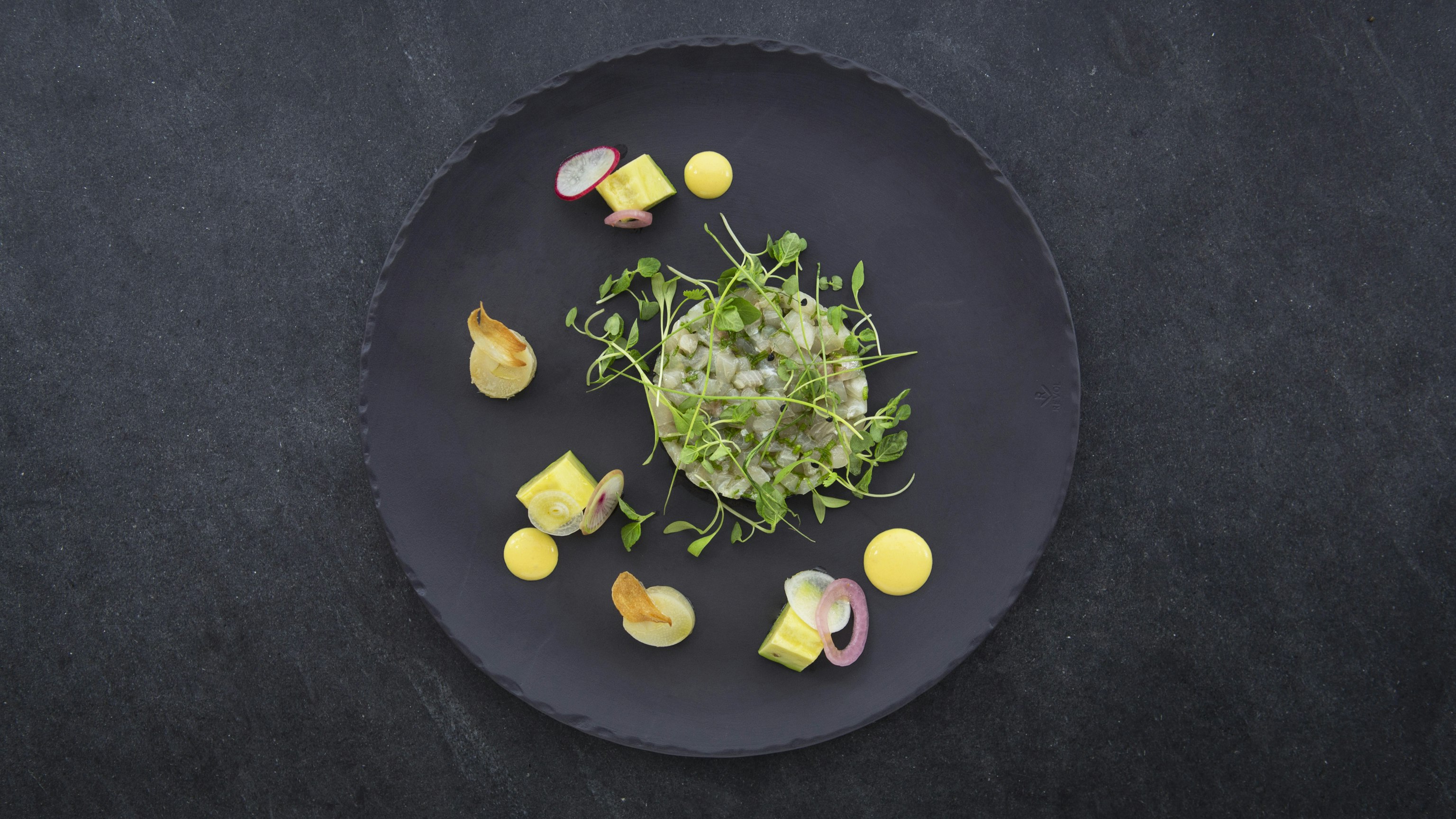 A round, gray slate plate with delicately presented morsels of food.