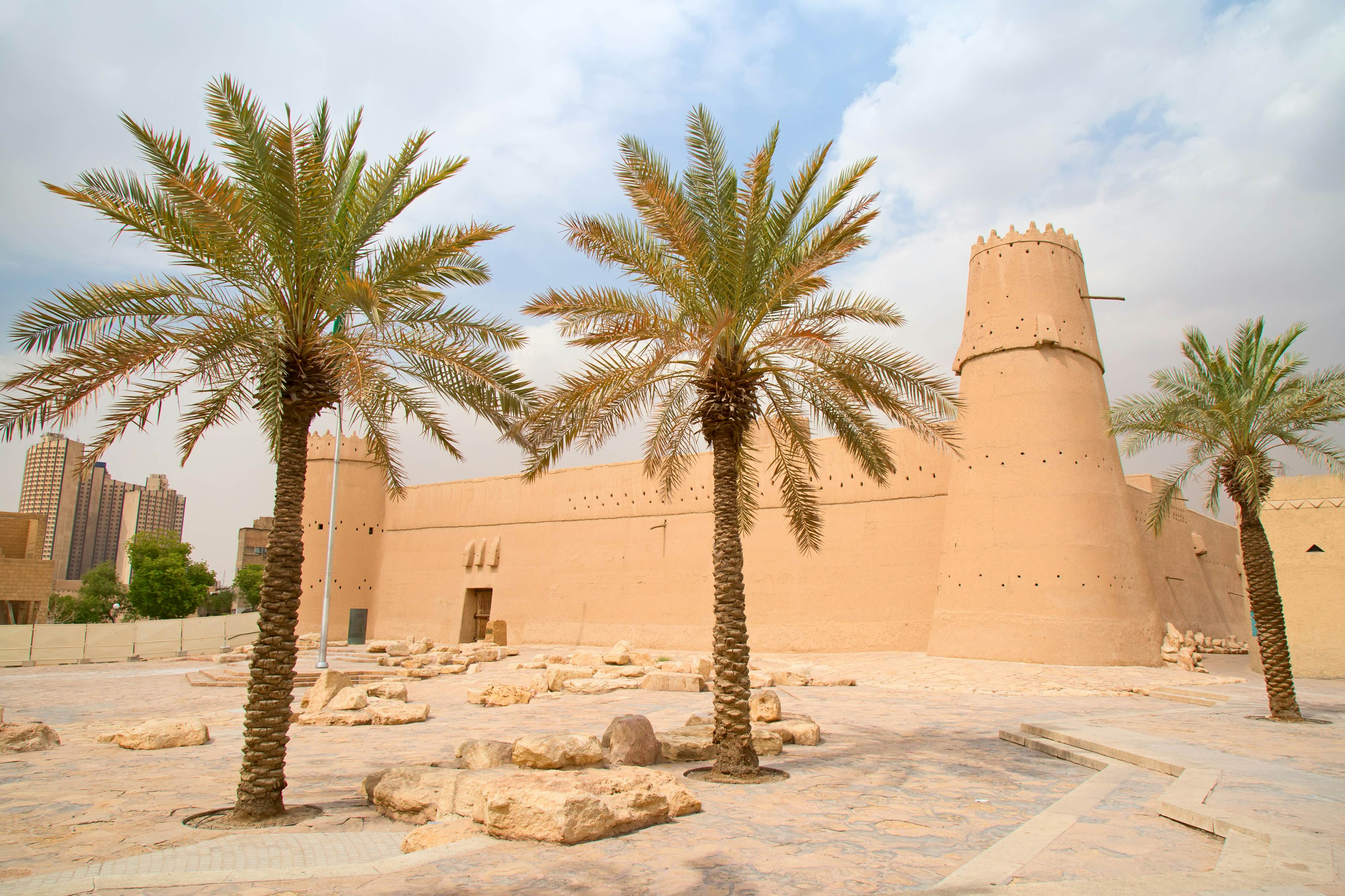 Sand-coloured fortress with palm trees in the foreground 