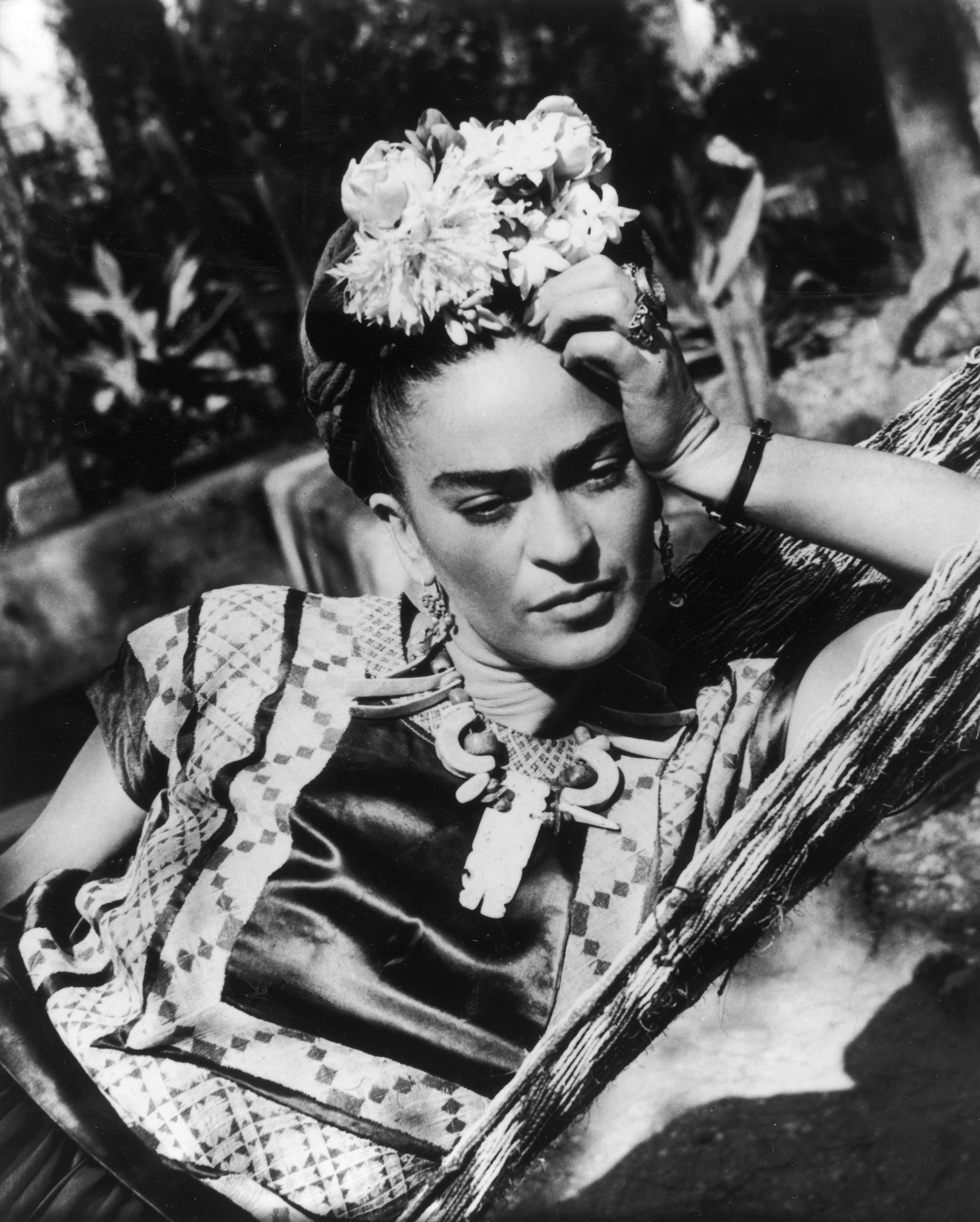 A black and white photo of Frida Kahlo, leaning to the side and propping up her head with her hand