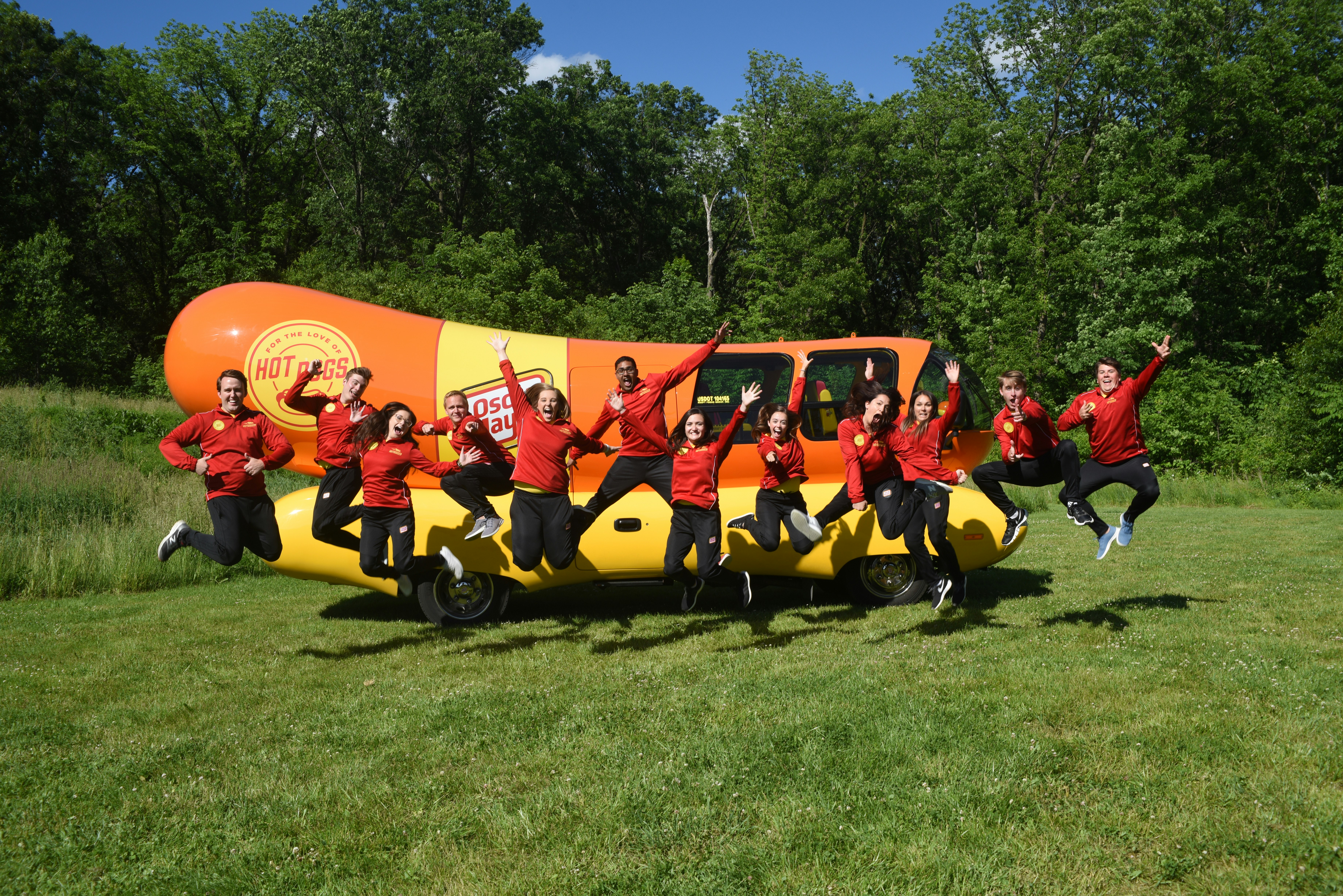 Oscar Mayer's 2019 Hotdoggers, wearing red shirts and black pants, jumping in front of the Wienermobile