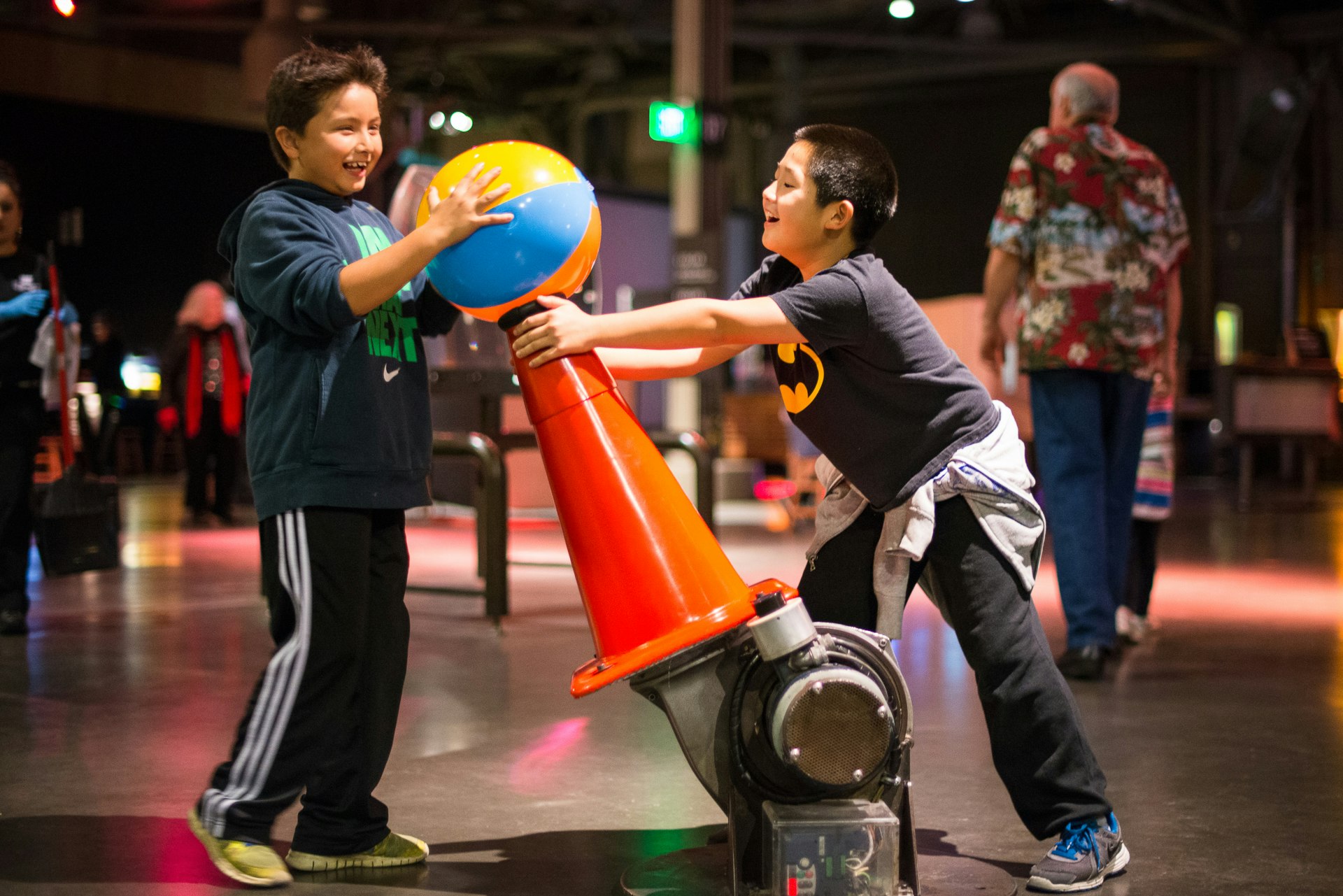 Two pre-teen boys are laughing as they hold an inflatable beach ball against an orange cone-like structure