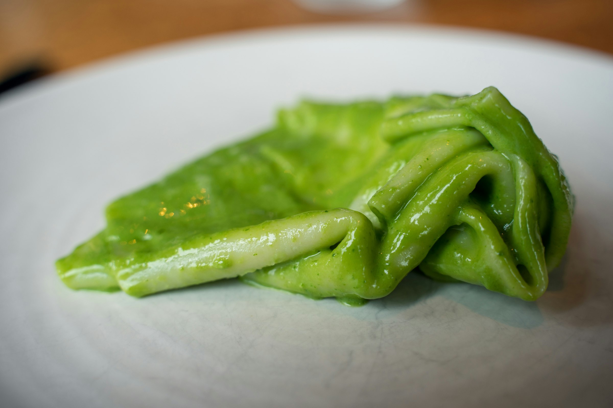A bright green tasting portion of Mandilli al Vero Pesto Genovese at Solo Italiano is shown in close up, gleaming on a white plate