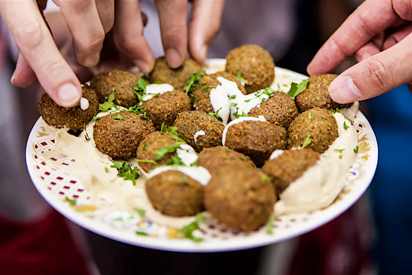falafel_sharjah.jpg Three hands are reaching to take a tasty-looking falafel from the collection on a plate.