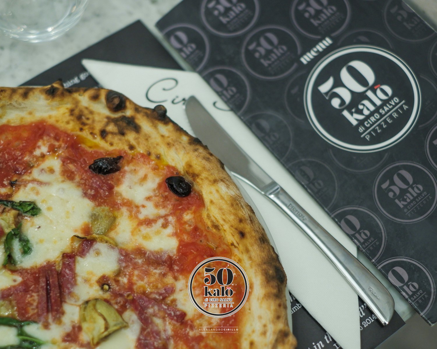 A picture of a pizza on a table with the 50 kalò menu